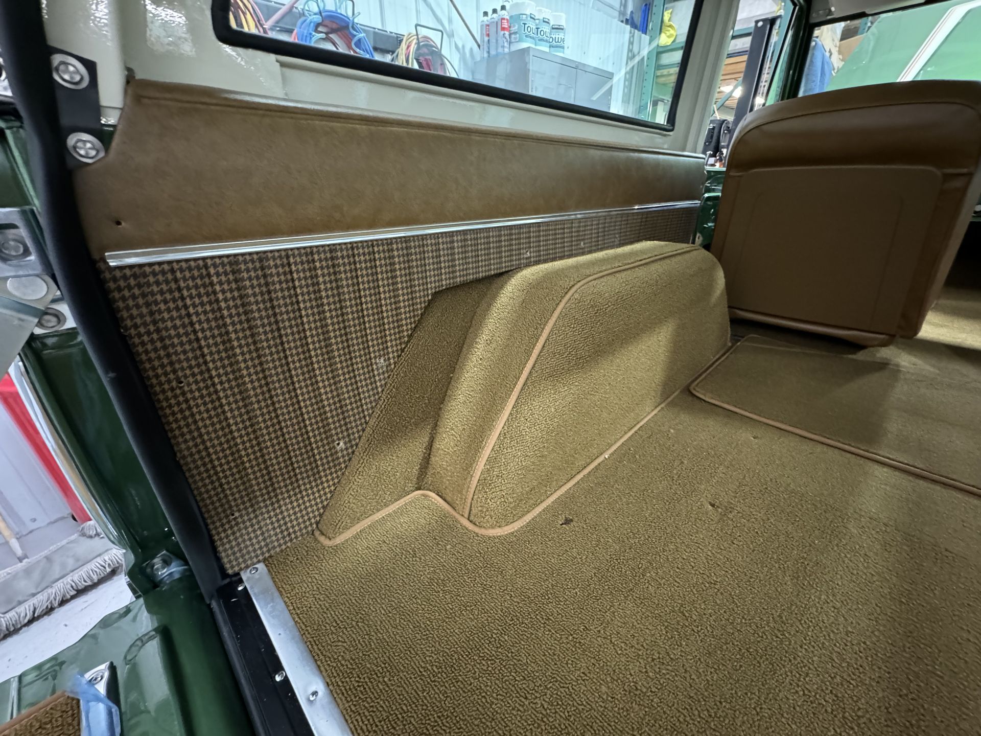 Car interior with tan carpeted floor, side panel, and window trim in a rear cargo area