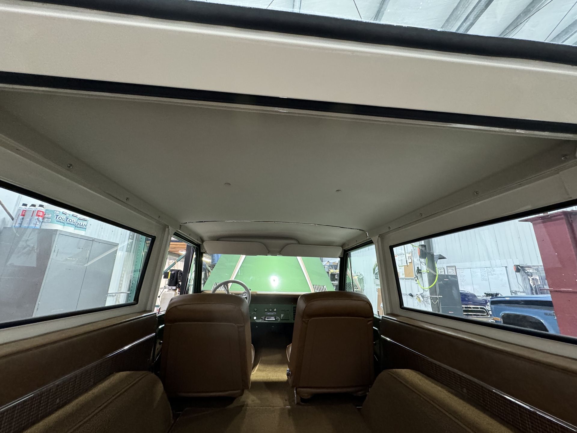 Inside a vintage car interior with tan seats, looking out through large windows at a street scene