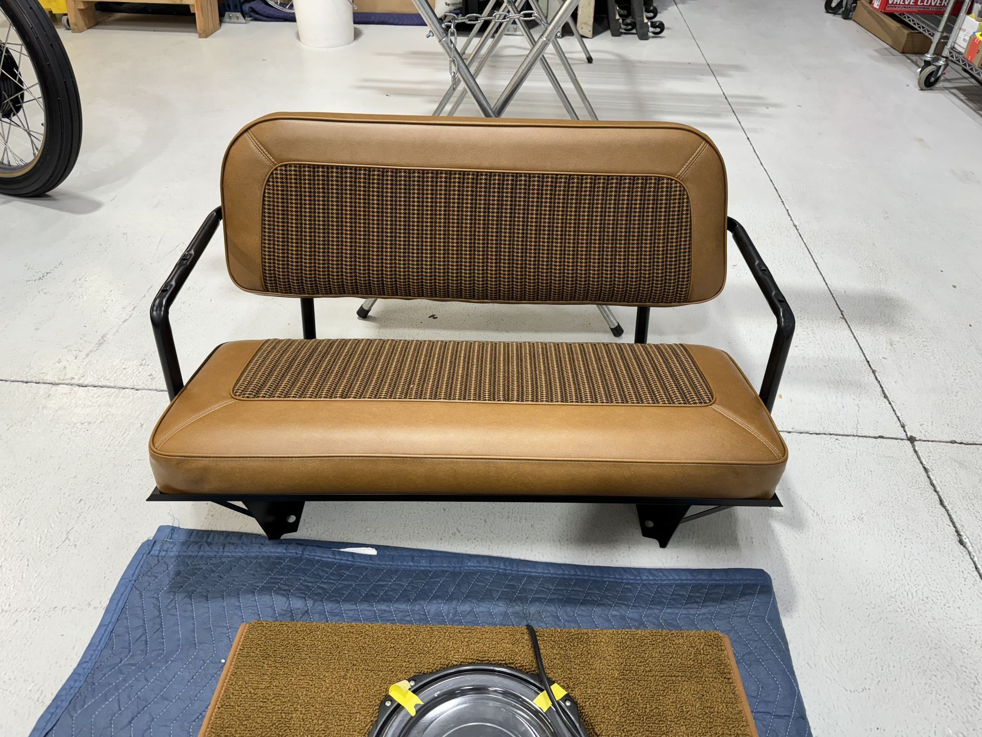 Brown bench seat in a workshop, with a blue mat and tools on the floor in front.