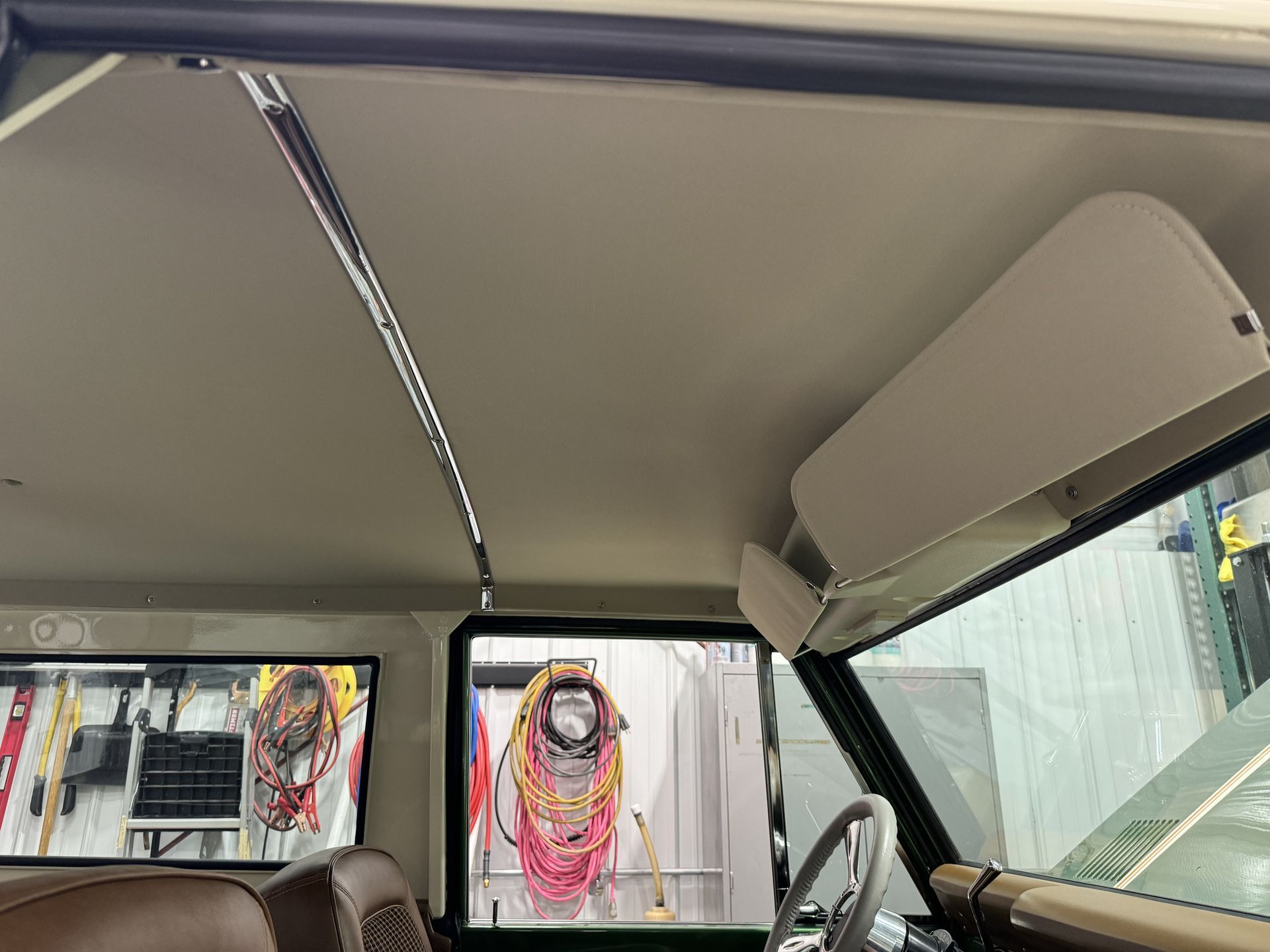 Interior view of a vehicle with an open roof, showing a garage and wall-mounted hoses outside.
