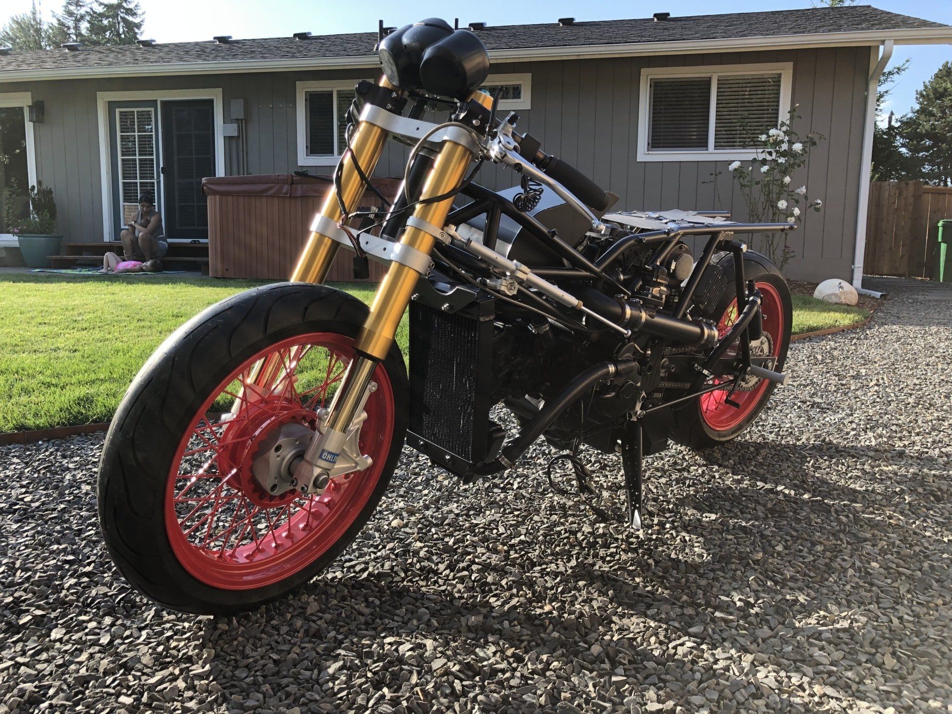 Custom black motorcycle with red wheels parked in front of a house on a gravel driveway