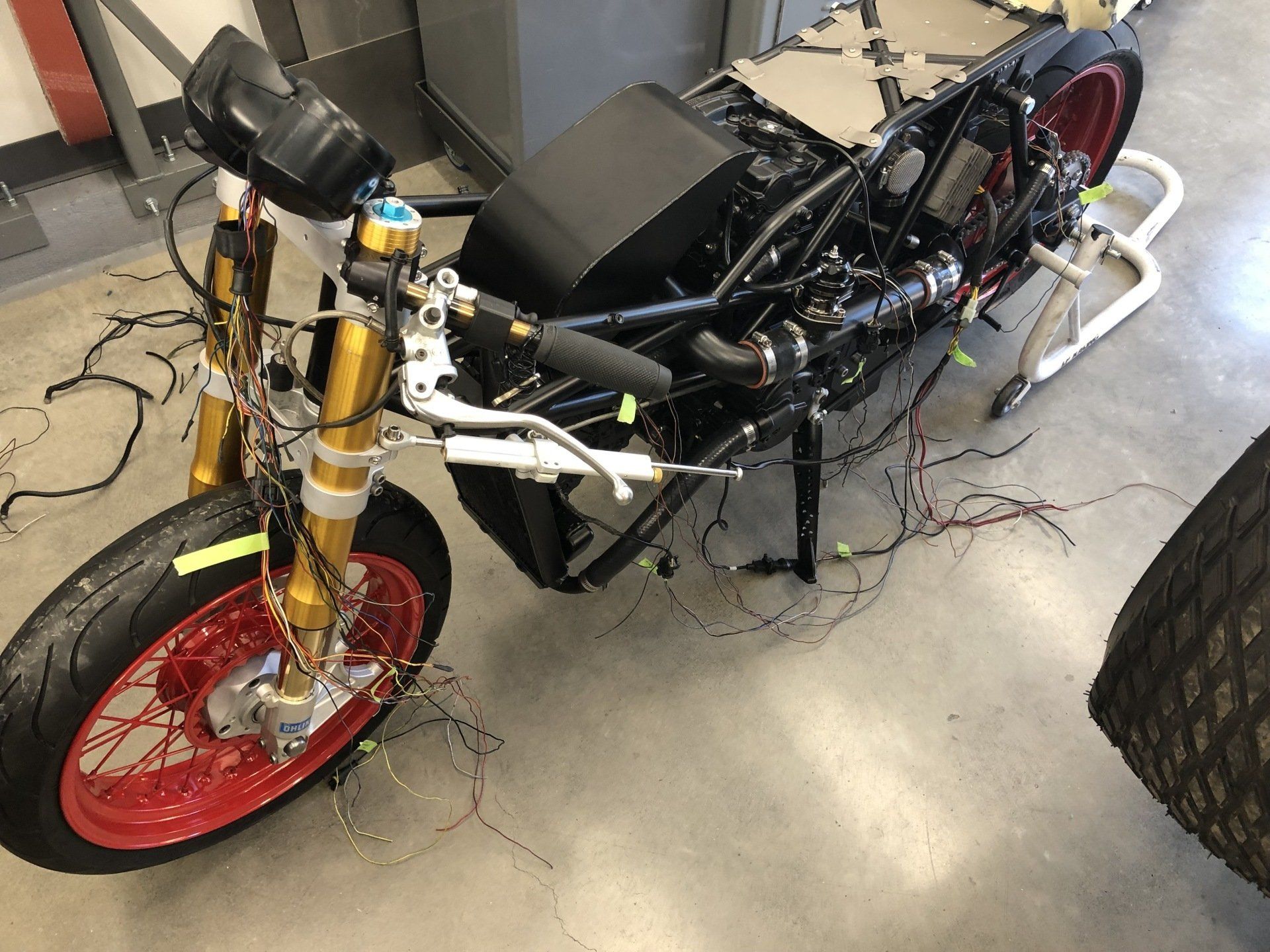 Open-wheel race car chassis in a garage, with a red front wheel and exposed components.
