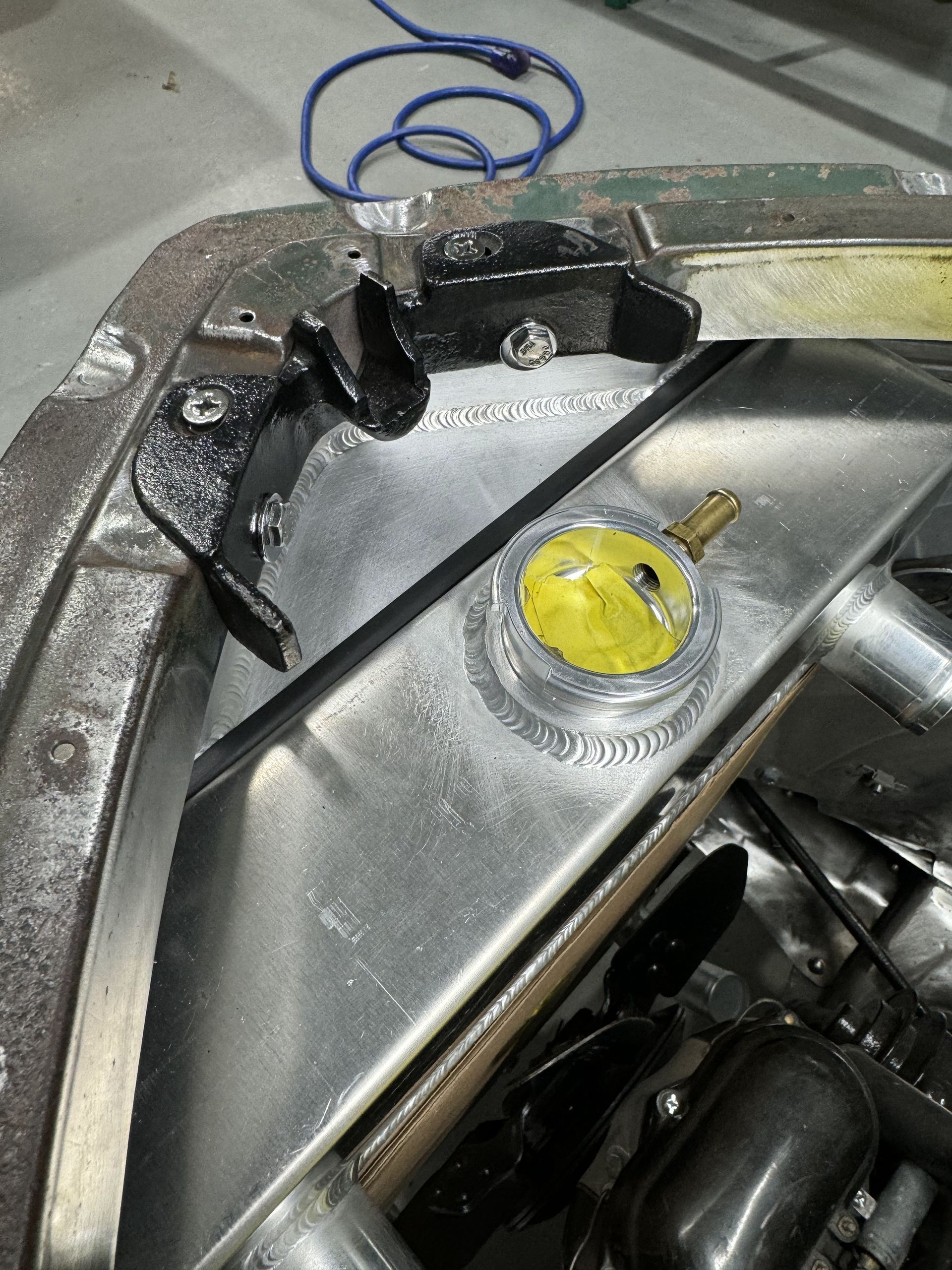 Close-up of a metal car body panel with wiring and a yellow cap inside the trunk area
