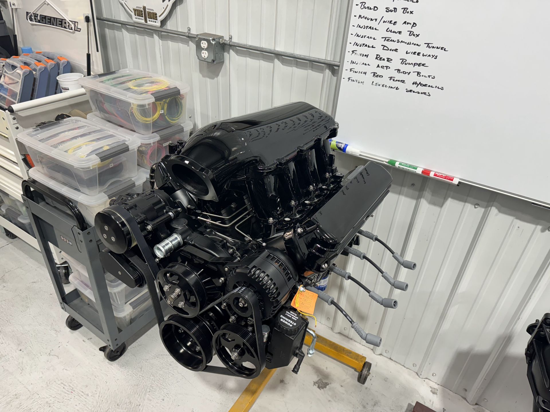 Black engine on a stand in a garage workshop, with tools and storage bins nearby.
