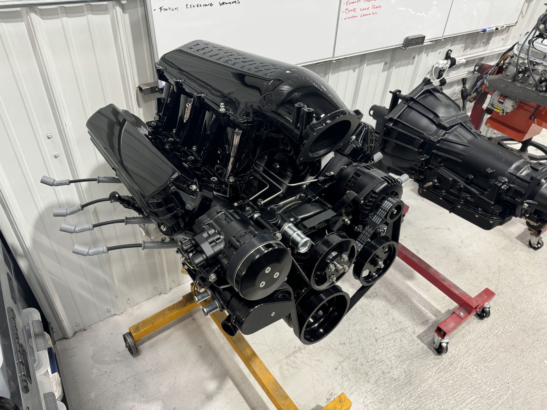 Black engine assembly on a stand in a workshop, with exposed components and hoses.