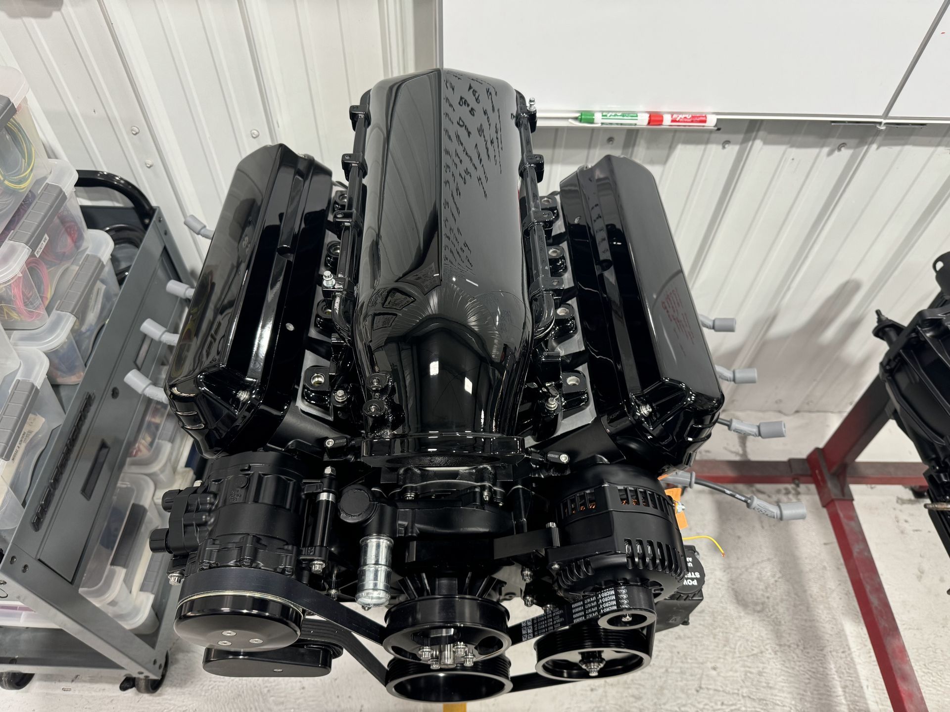 Black engine block on a pallet in an industrial warehouse, with hoses and metal components attached
