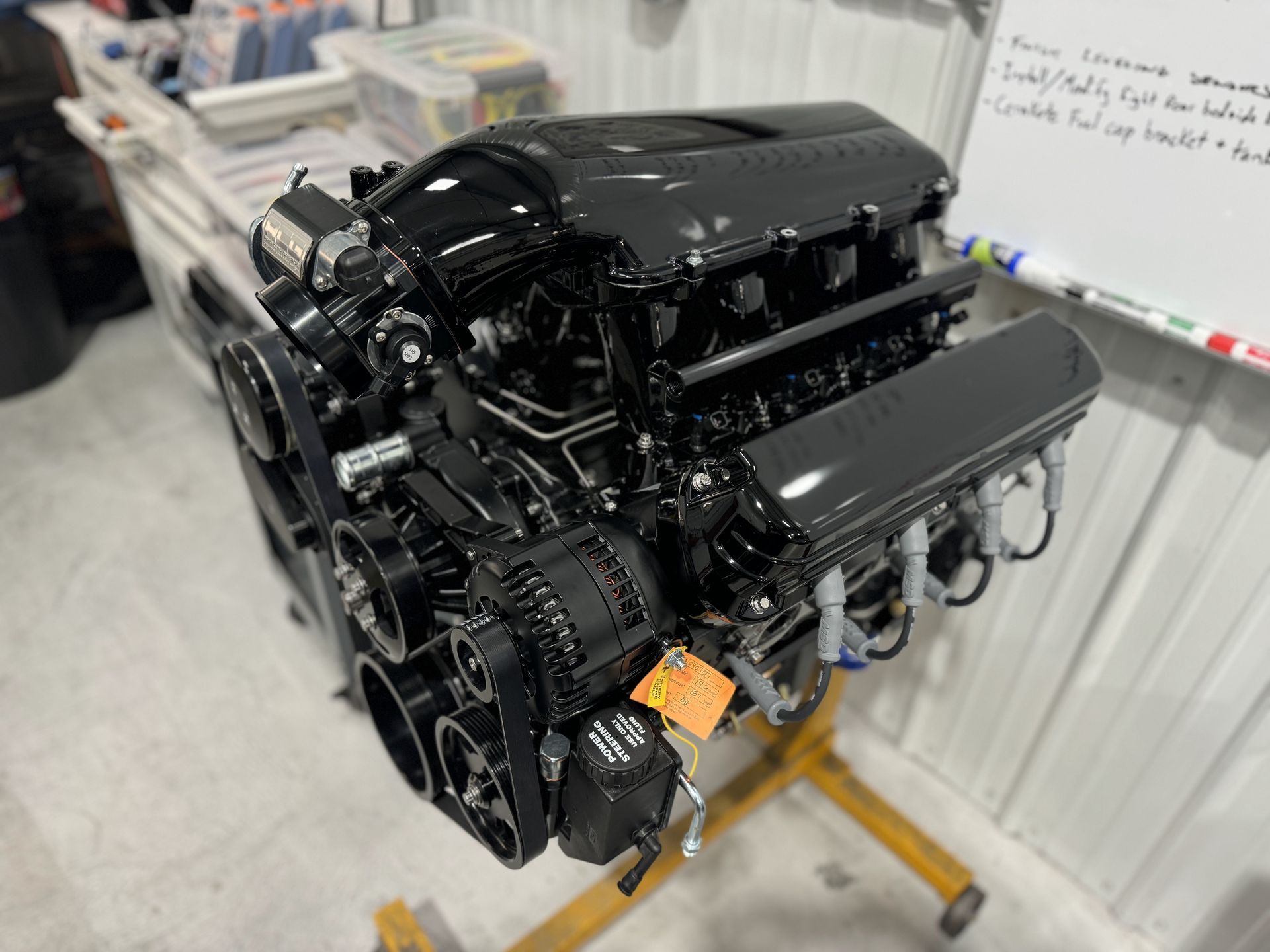 Black engine on a yellow stand in a workshop, with a whiteboard in the background