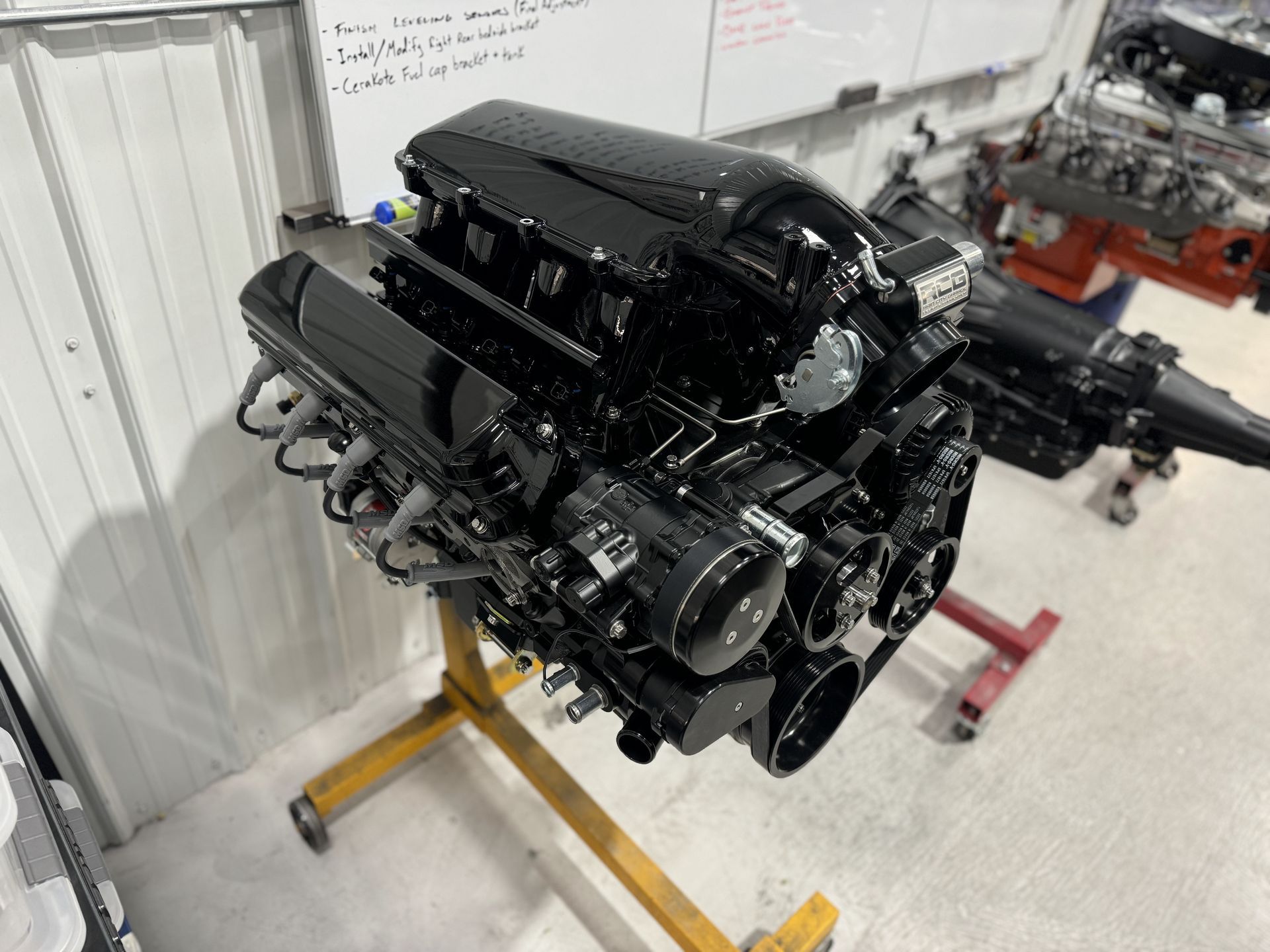 Black V8 engine on a stand in a workshop, with exhaust headers and intake visible
