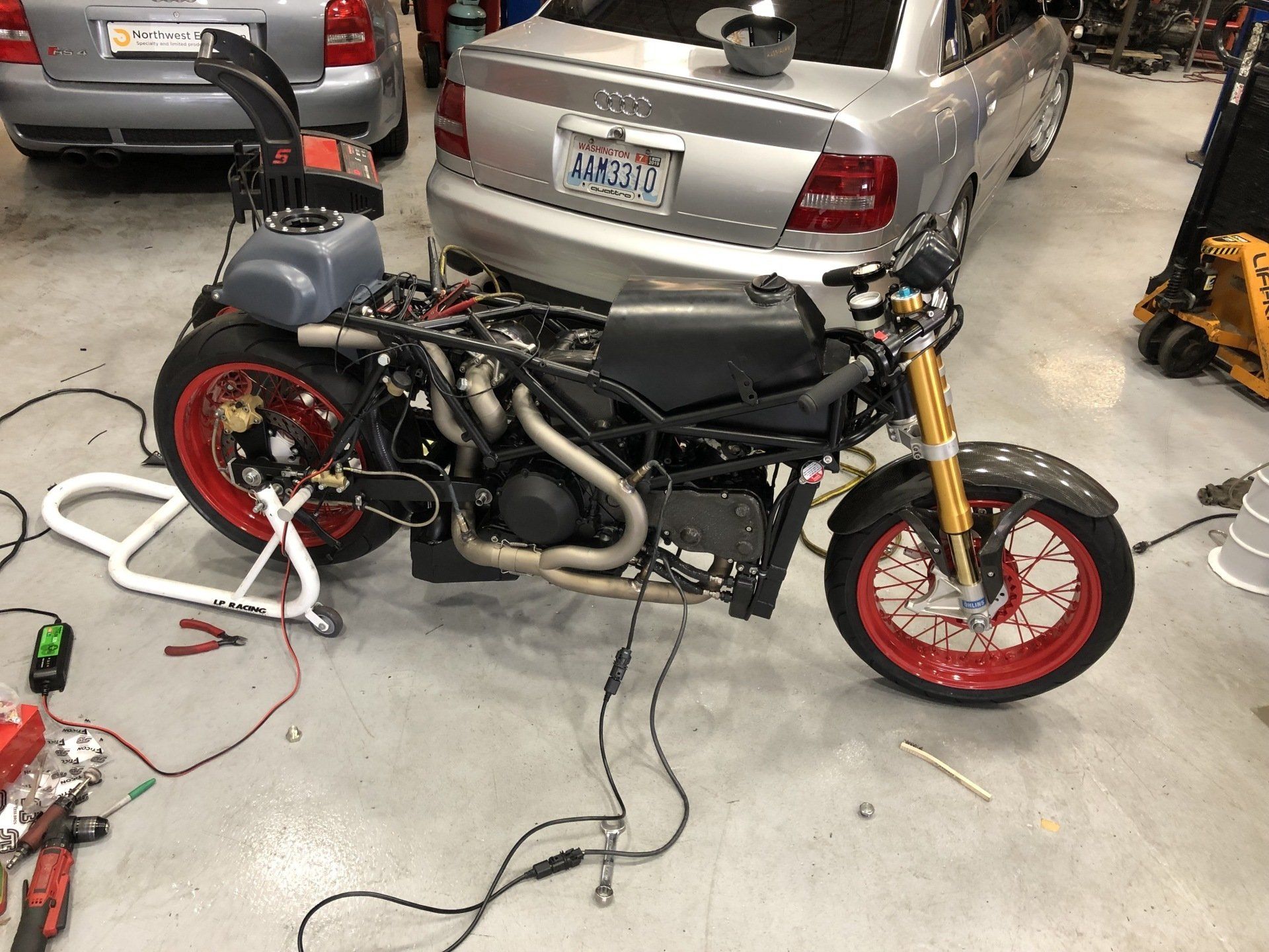 Custom motorcycle with red wheels in a garage beside parked cars and tools on the floor