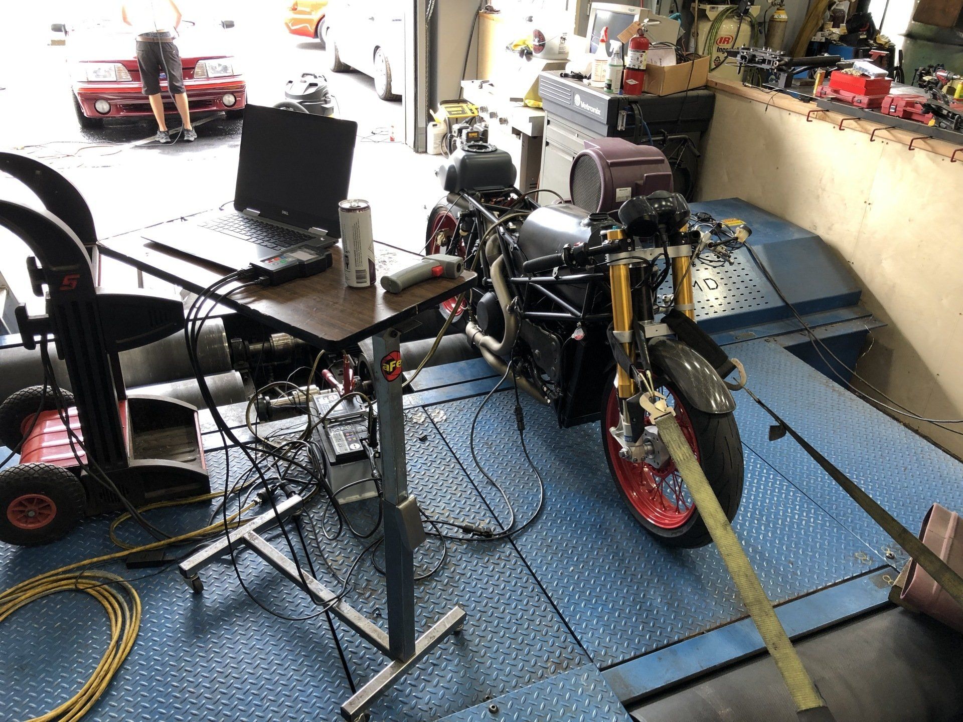Cluttered garage with several bicycles, tools, and a blue motorcycle on the floor near a workbench.