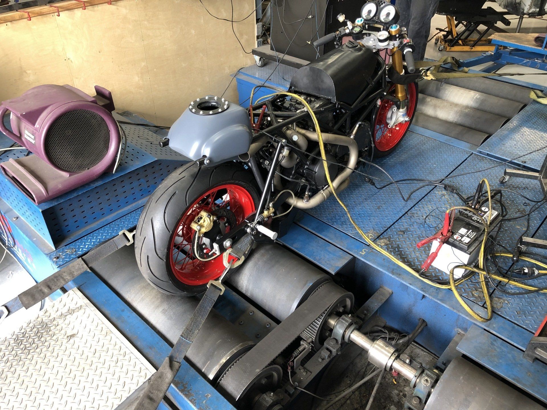 Customized motorcycle on a blue platform, with red wheels and exposed engine parts in a workshop.