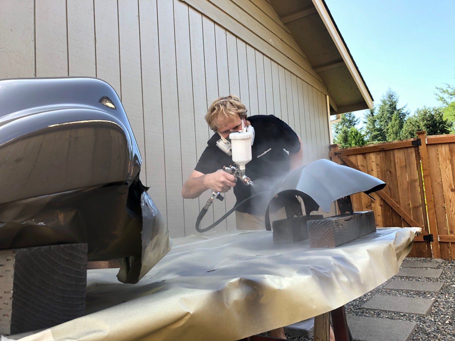 Person power-sanding a boat hull outdoors, with dust and a trailer nearby