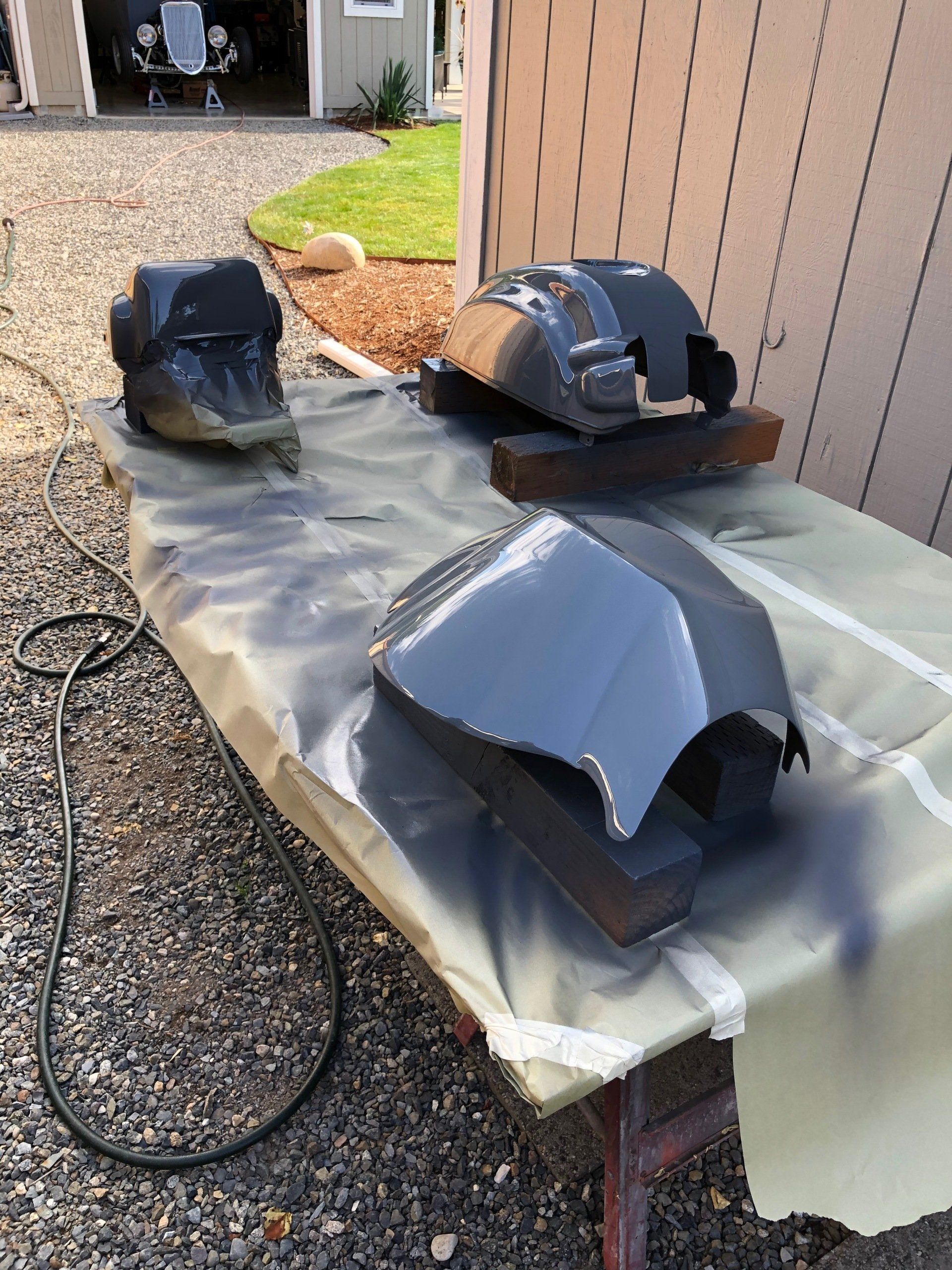 Three dark metal roof vents on a tarp-covered table outdoors by a garage