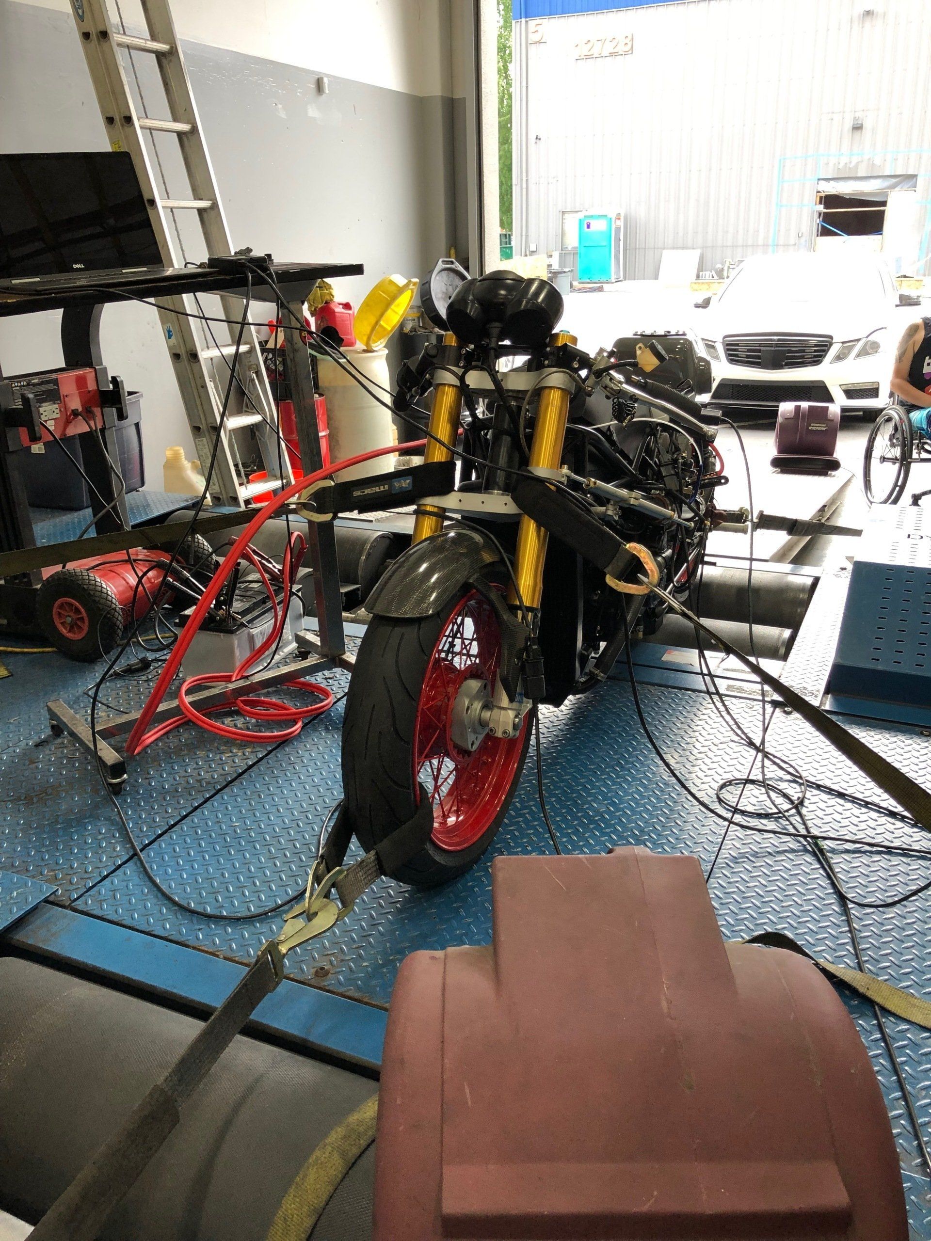 Yellow-and-red motorcycle on a blue shop floor inside a garage, with tools and equipment nearby