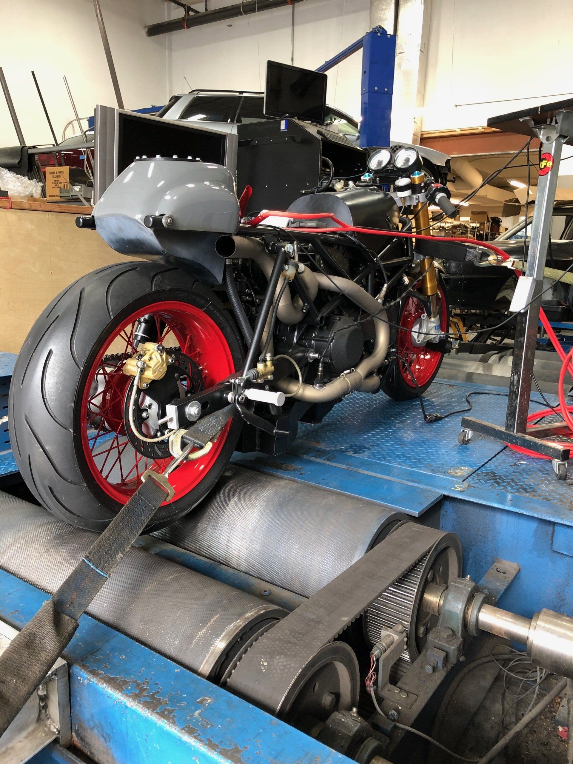 Motorcycle on a dynamometer in a garage, with a red rear wheel and exposed engine.