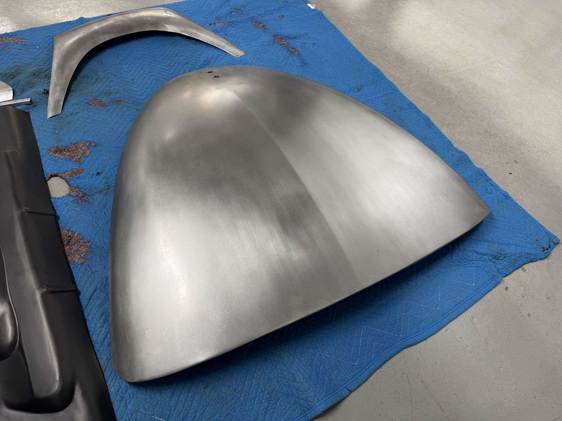 Metal car body panel on a blue mat beside other automotive parts in a workshop