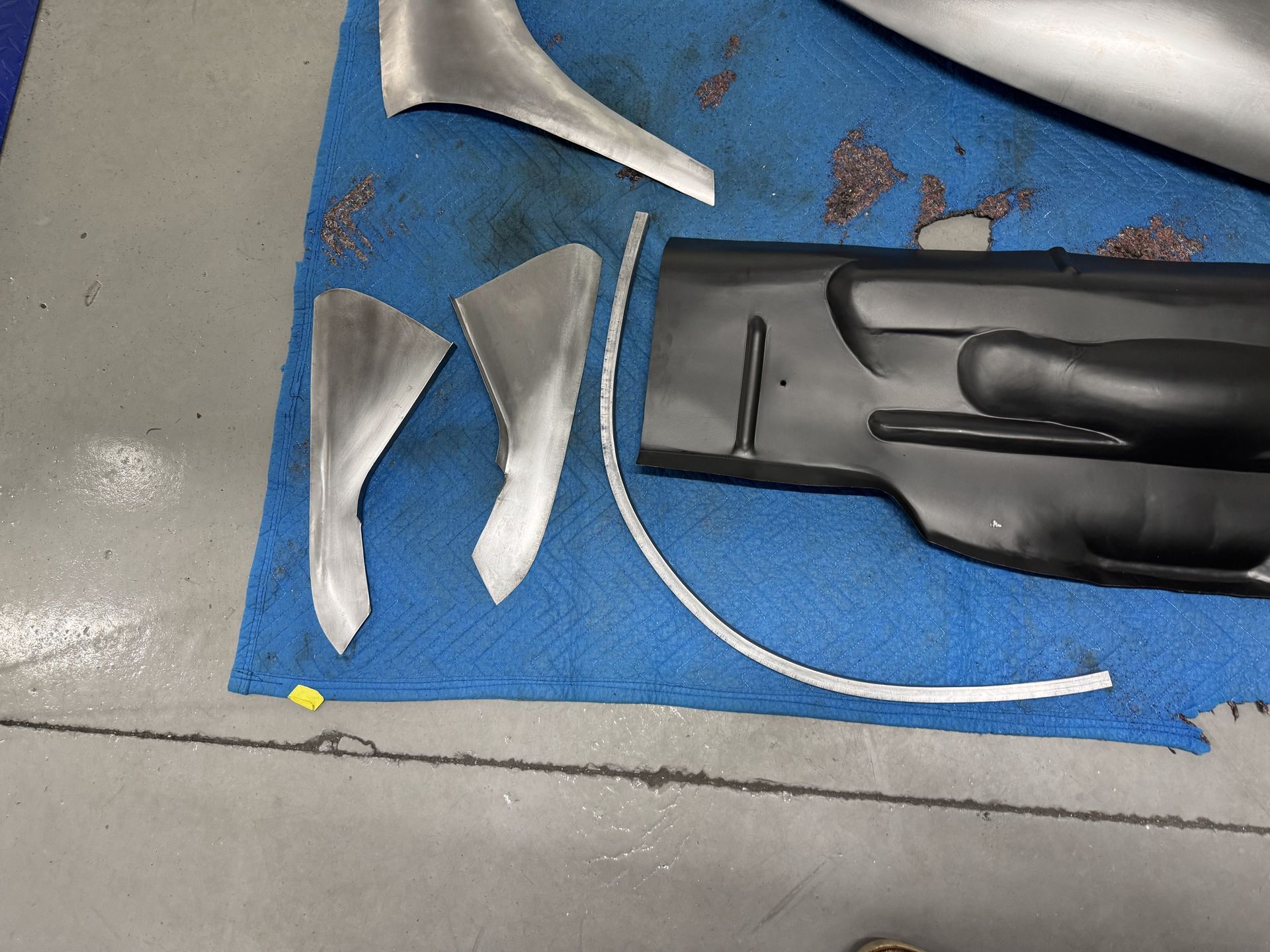 Blue mat with several metal tool parts and a black handle on a gray floor