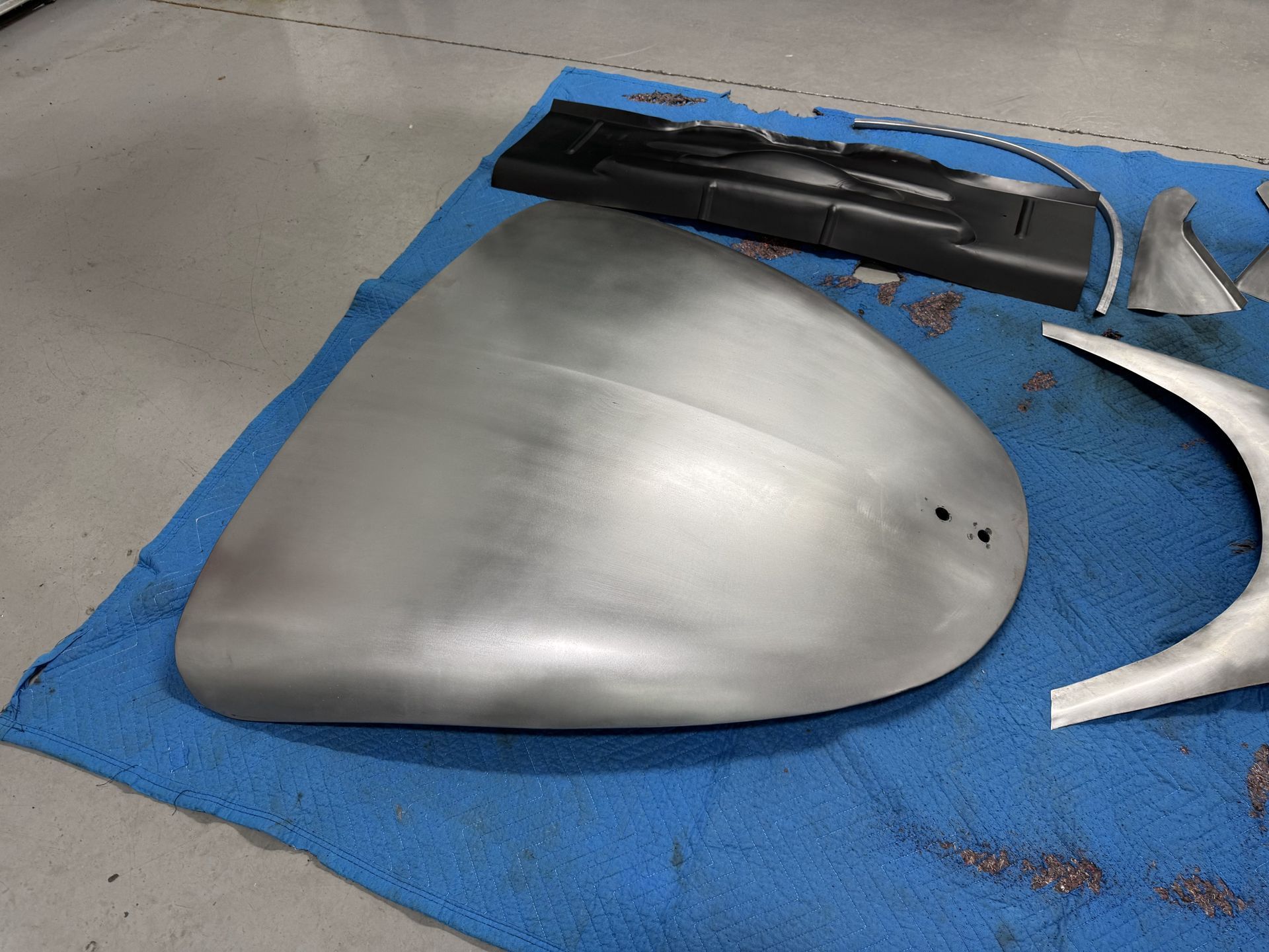 Silver car mirror cover on a blue mat with black and white trim pieces nearby