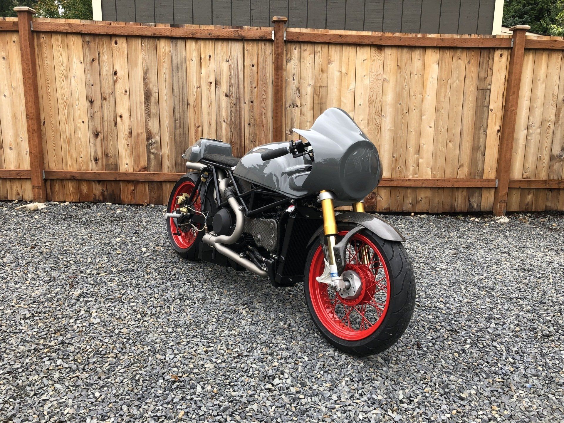 Black sport motorcycle with red wheels parked on gravel in front of a wooden fence.