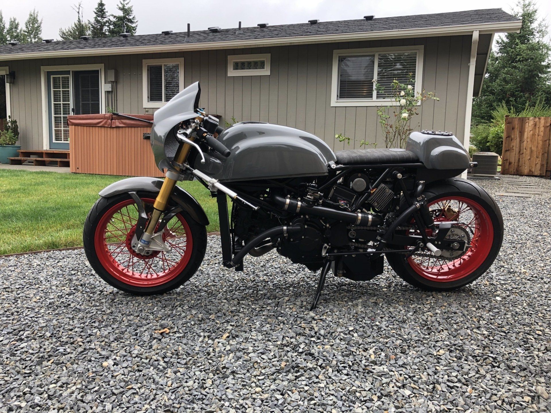 Black motorcycle with red rims parked on gravel in front of a small gray house