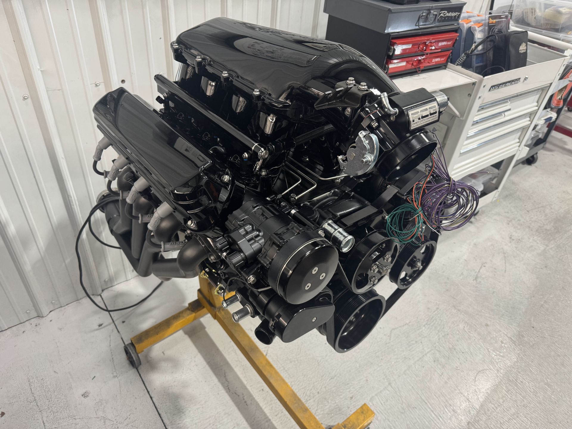 Black car engine mounted on a stand in a workshop, with tool cabinets in the background