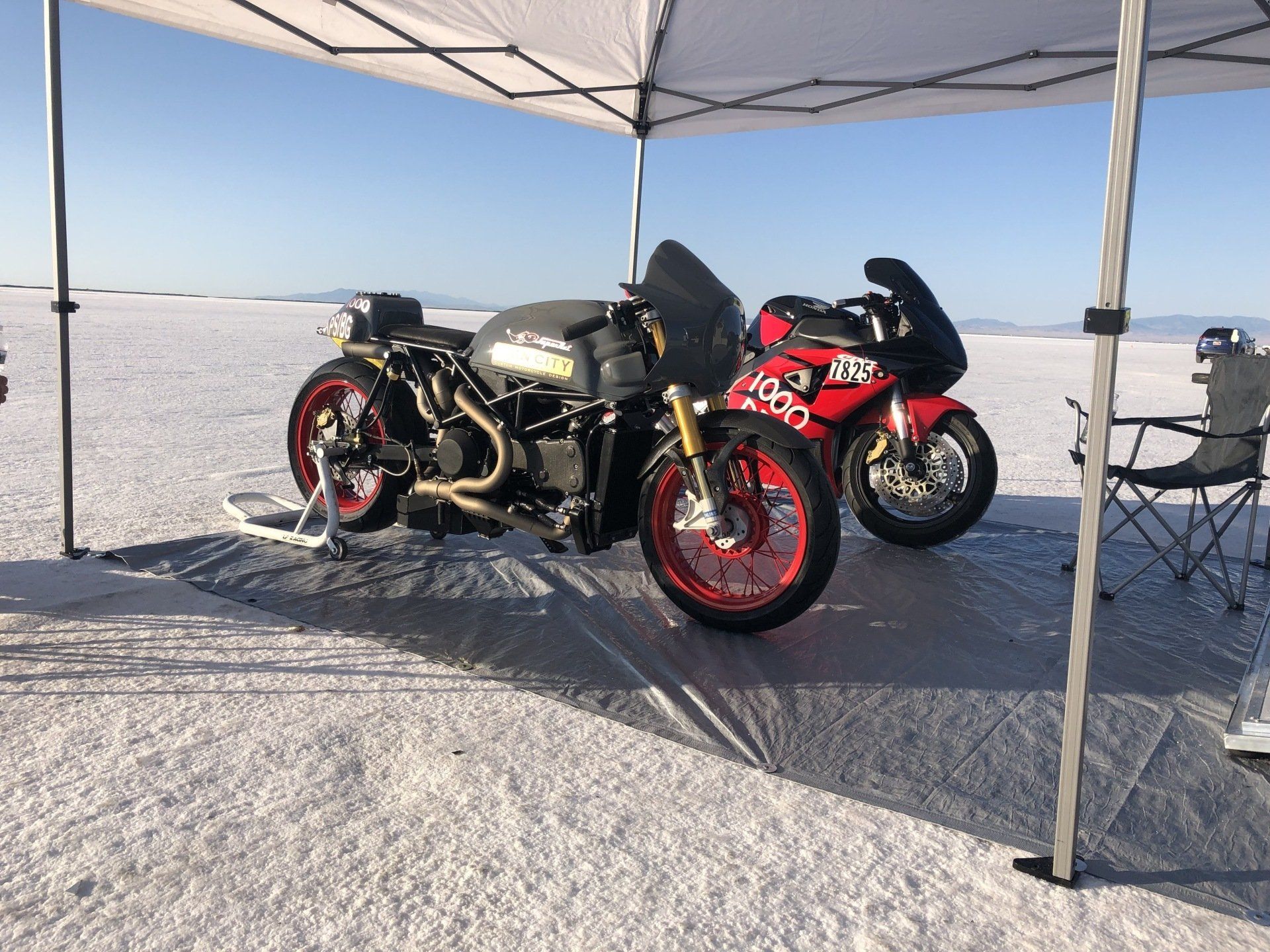 Two sport motorcycles under a canopy on a snowy flat landscape, one black and one red.