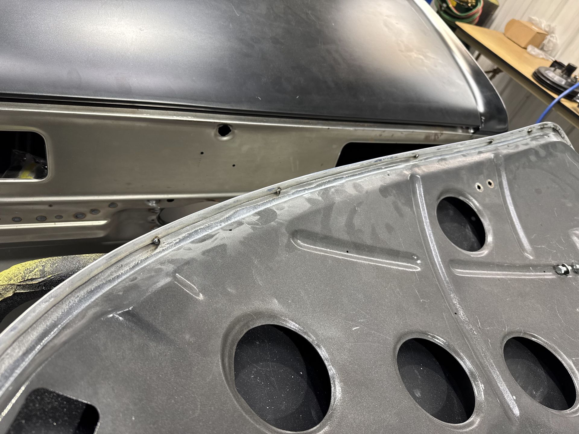 Close-up of a gray car body panel with round cutouts in a workshop