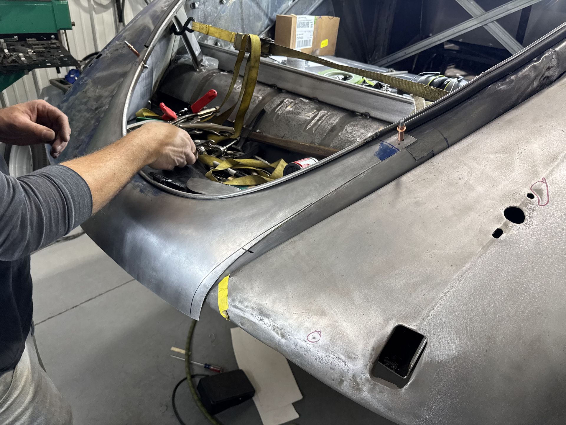 Hands repairing a damaged gray fabric seat cushion inside a workshop, with exposed stuffing visible