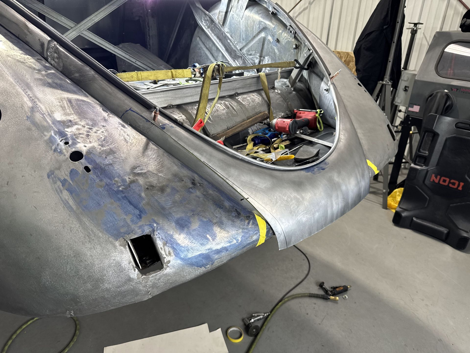 Gray damaged aircraft fuselage in a workshop, with exposed wiring and tools inside the cockpit area.