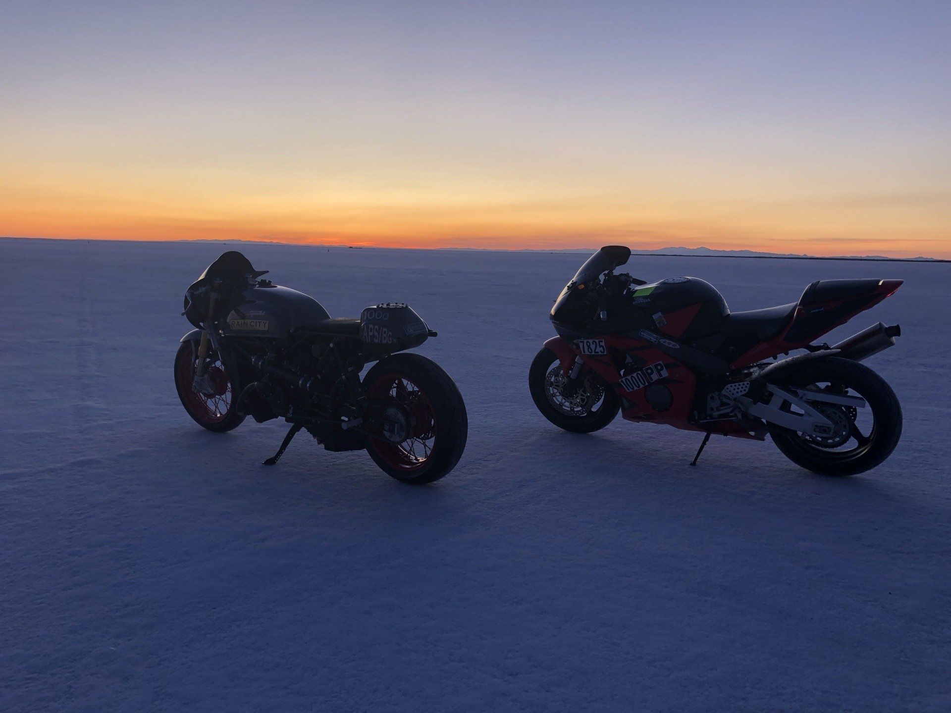 Two sport motorcycles parked on a snowy plain at sunset