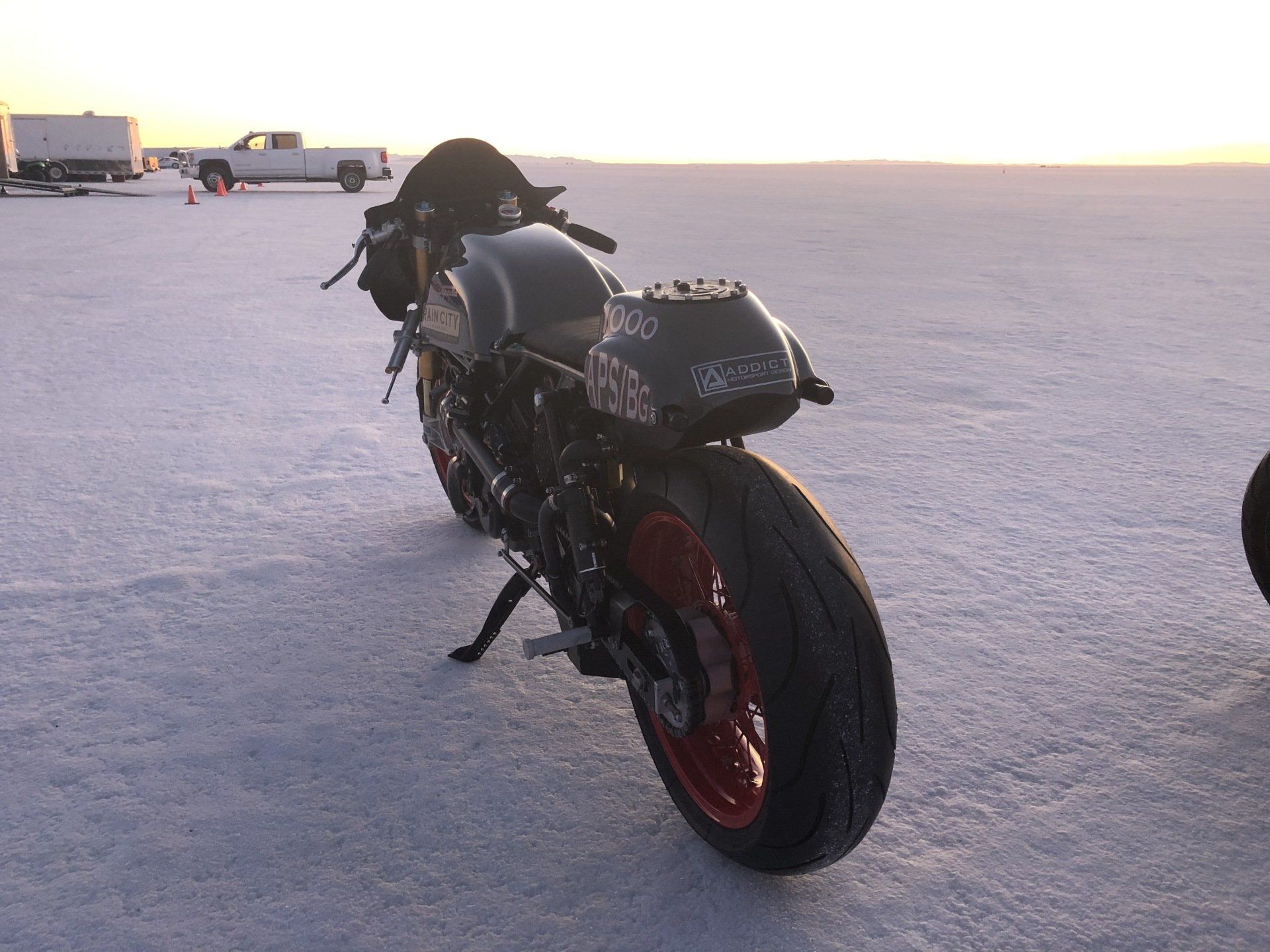 Black sport motorcycle with red rims parked on a snowy lot at sunset