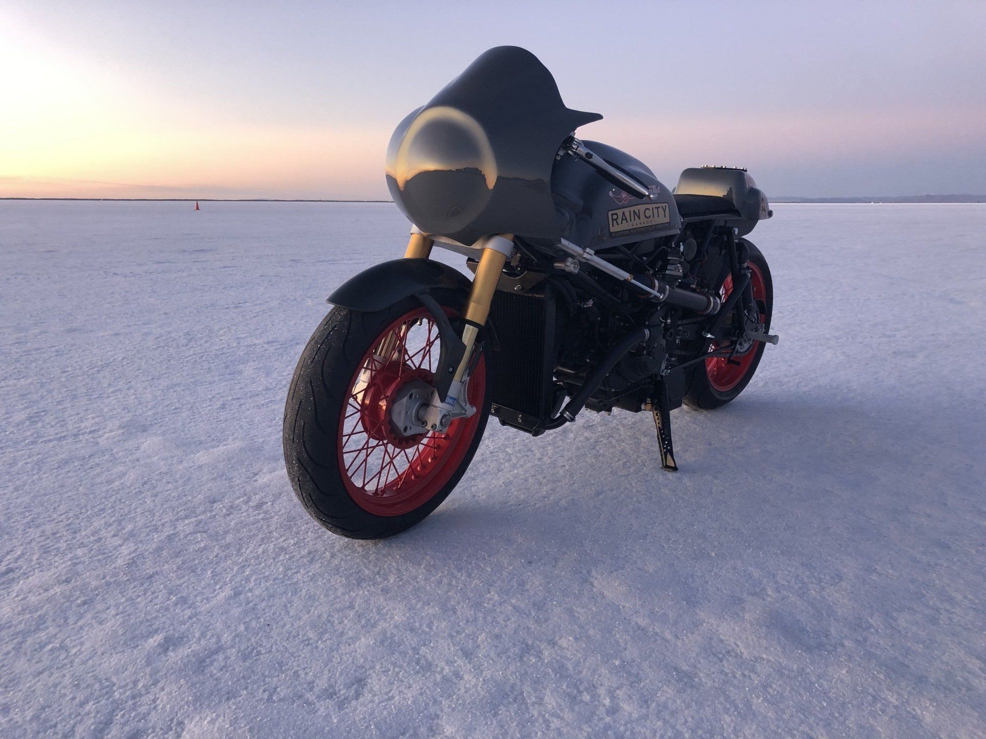 Black sport motorcycle with red wheels parked on a snowy plain at sunset.