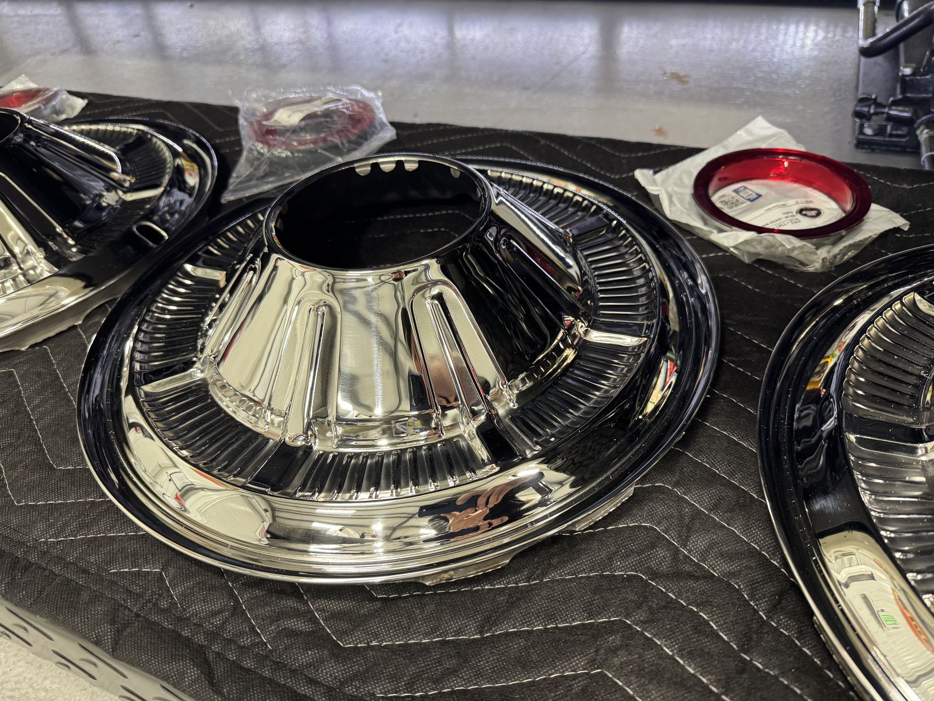 Chrome car air filter components on a quilted black mat, with a red-rimmed part nearby
