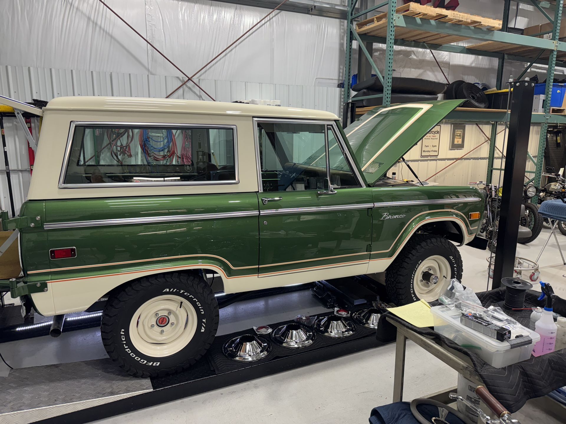 Green vintage SUV with hood open in a garage workshop, viewed from the side.