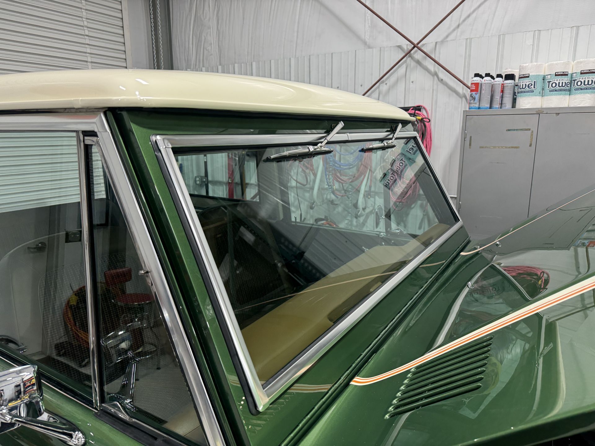 Green vintage car in a garage, showing the windshield, roof, and hood area