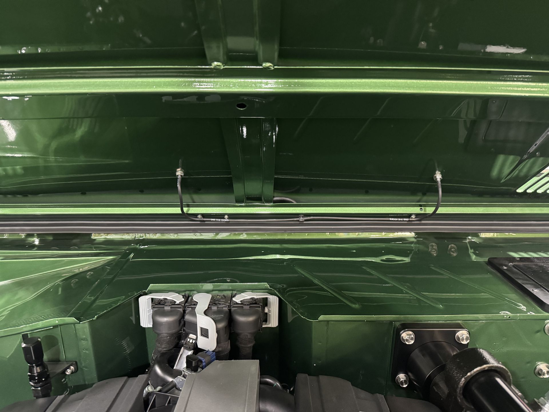 Green metal machinery with hoses and black fittings inside a vehicle or equipment compartment