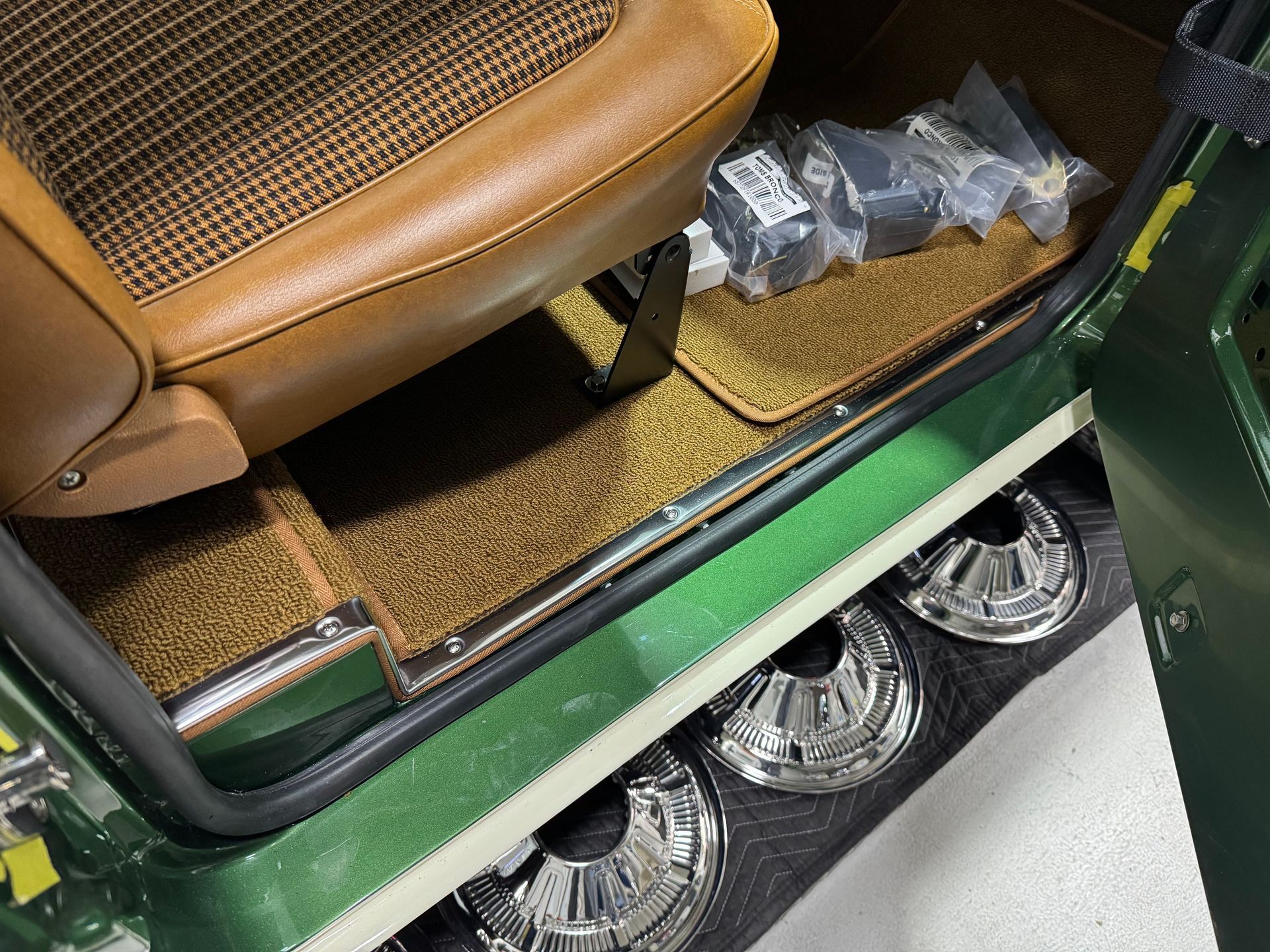 Brown car seat with a green body panel and shiny chrome wheels, viewed from inside the vehicle.