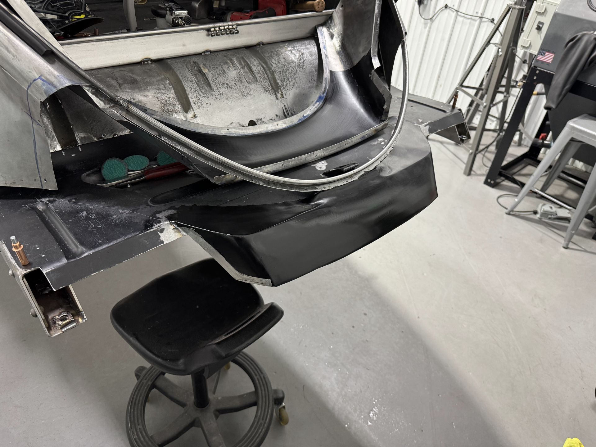 Workbench with a black curved metal panel and a rolling stool in a workshop setting