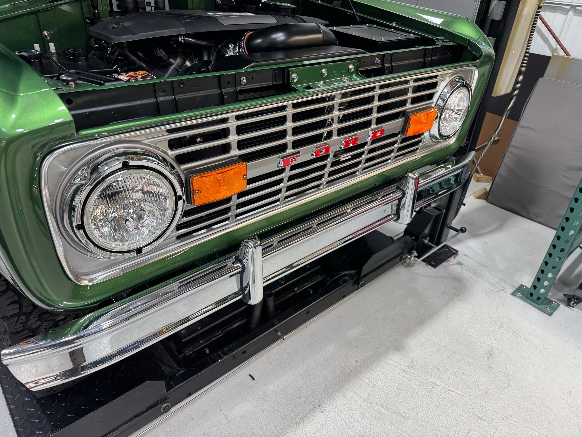 Close-up of a green classic truck front with chrome grille and round headlight in a garage.