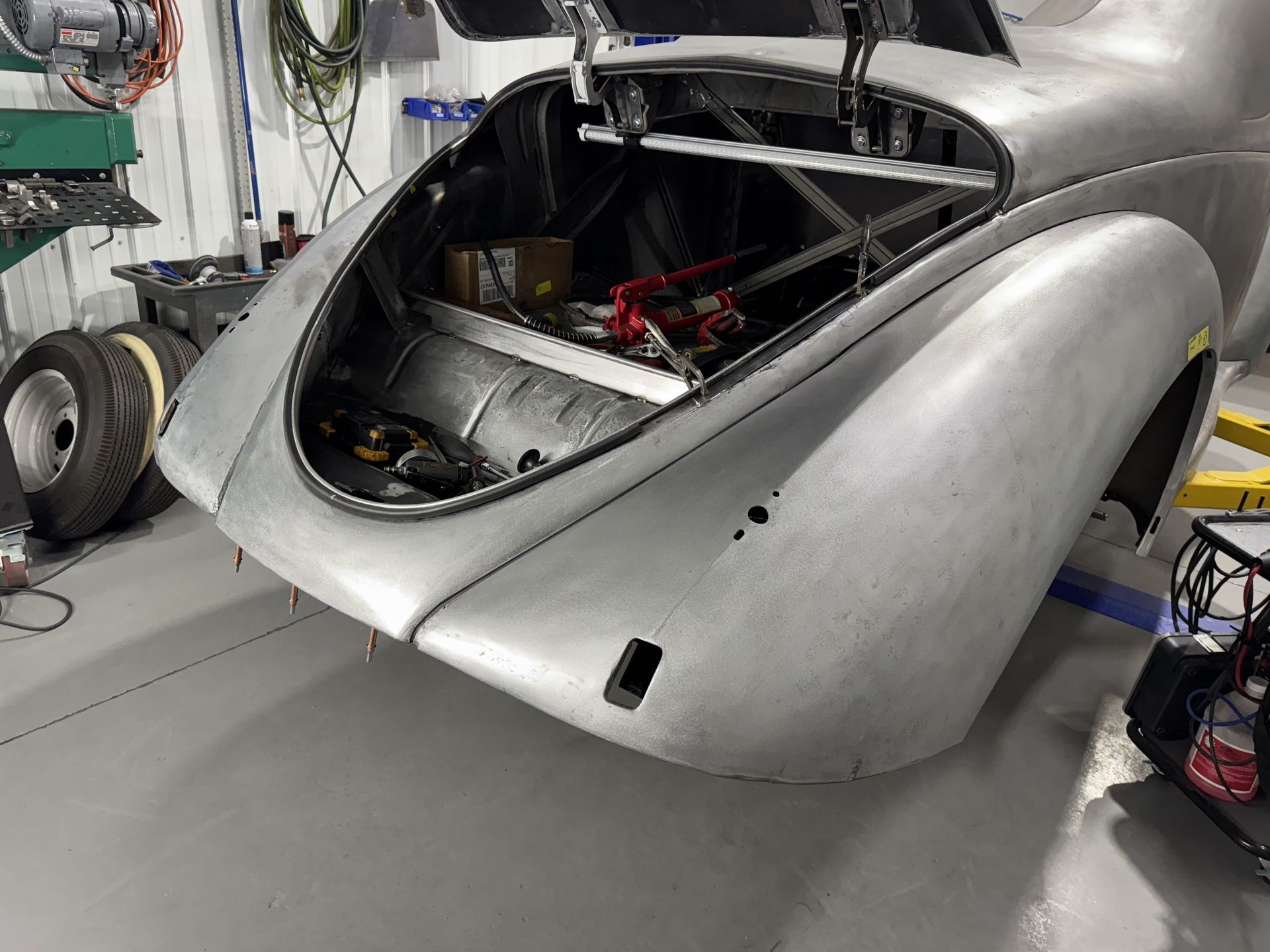 Silver vintage car body in a garage, viewed from the rear with the engine compartment open.