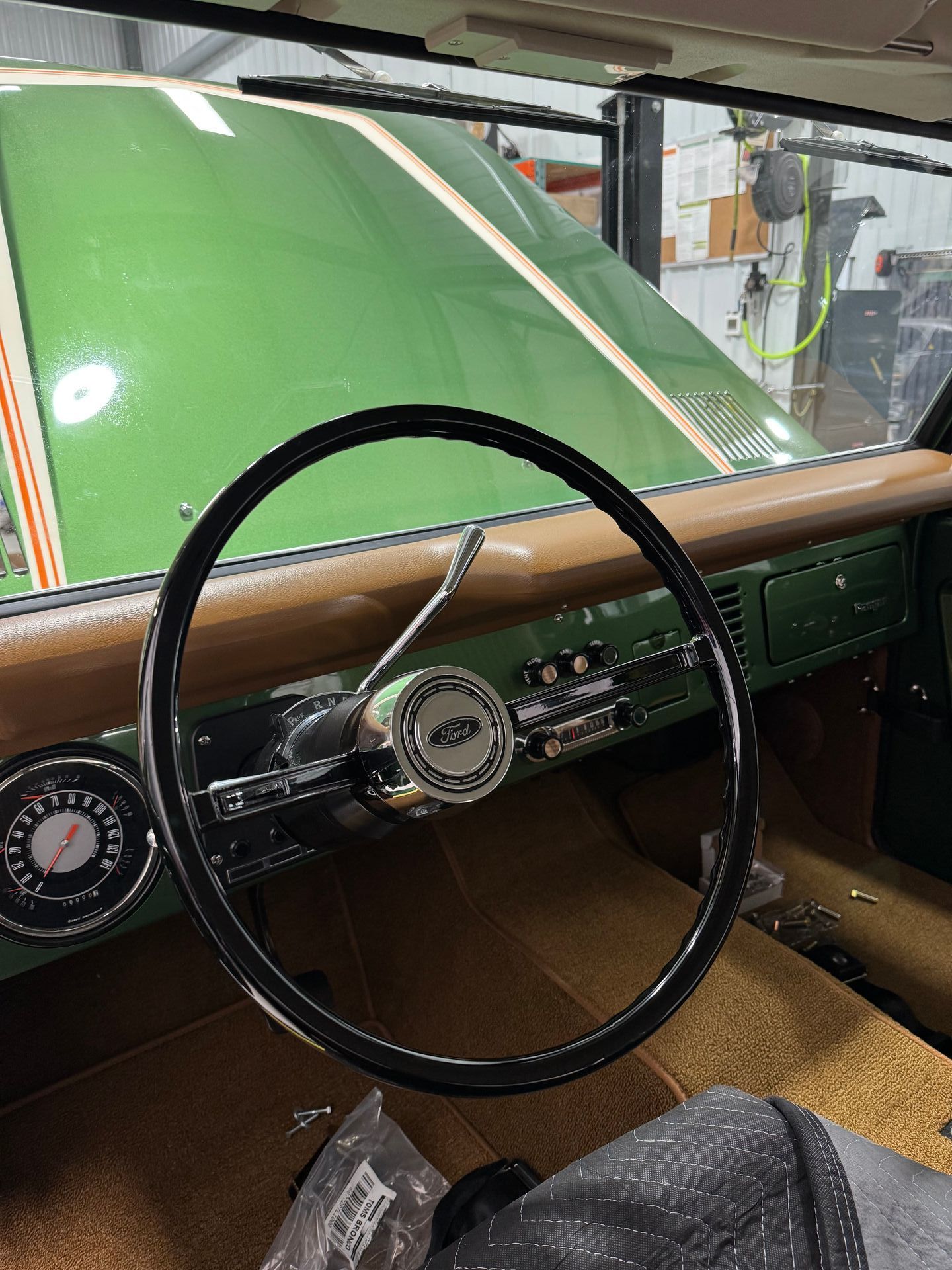 Classic car interior with black steering wheel and green hood visible through the windshield