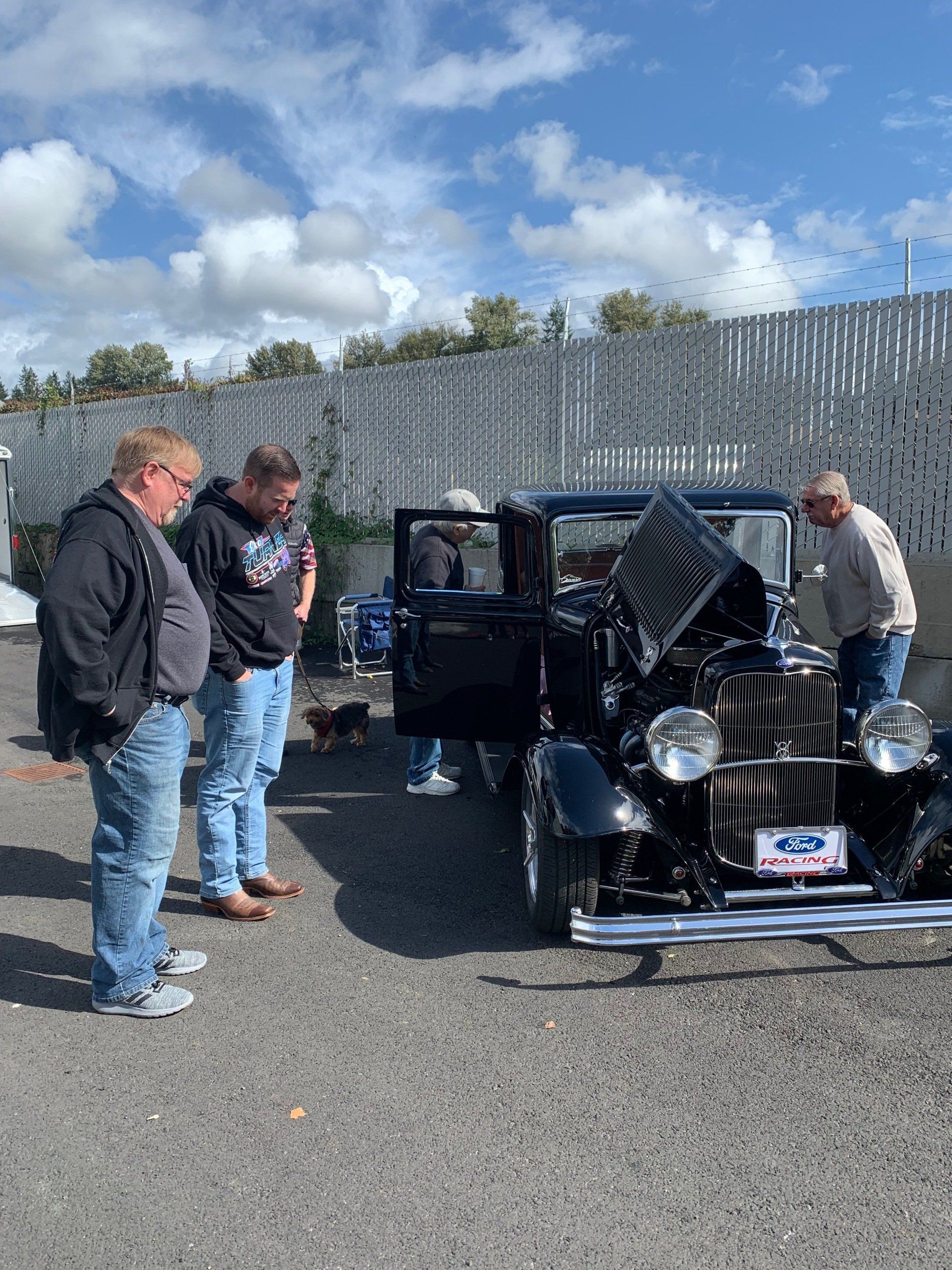 People inspecting a shiny black vintage car at an outdoor car show on a sunny day