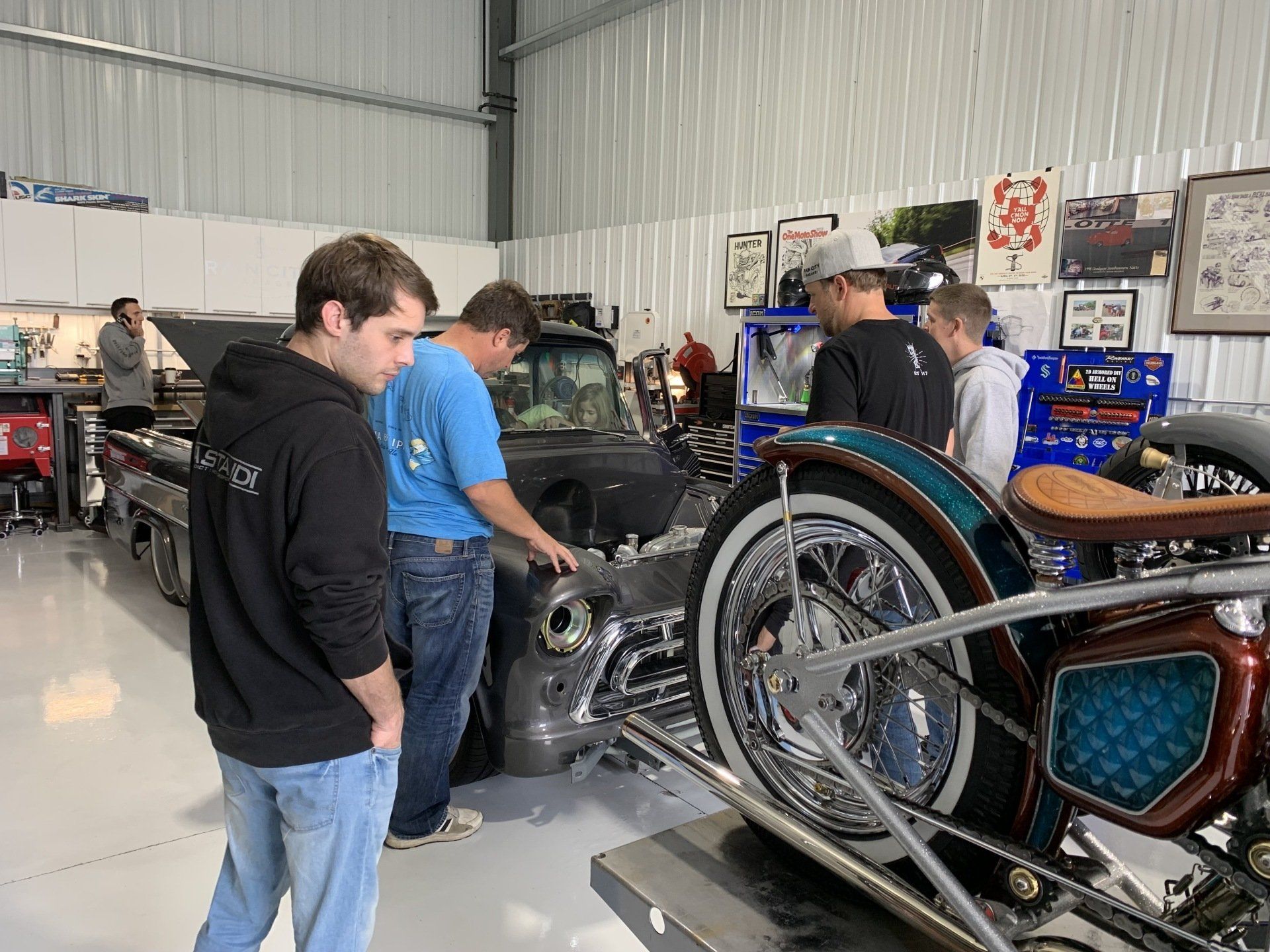 People examining a large custom motorcycle in a workshop with tools and machinery.