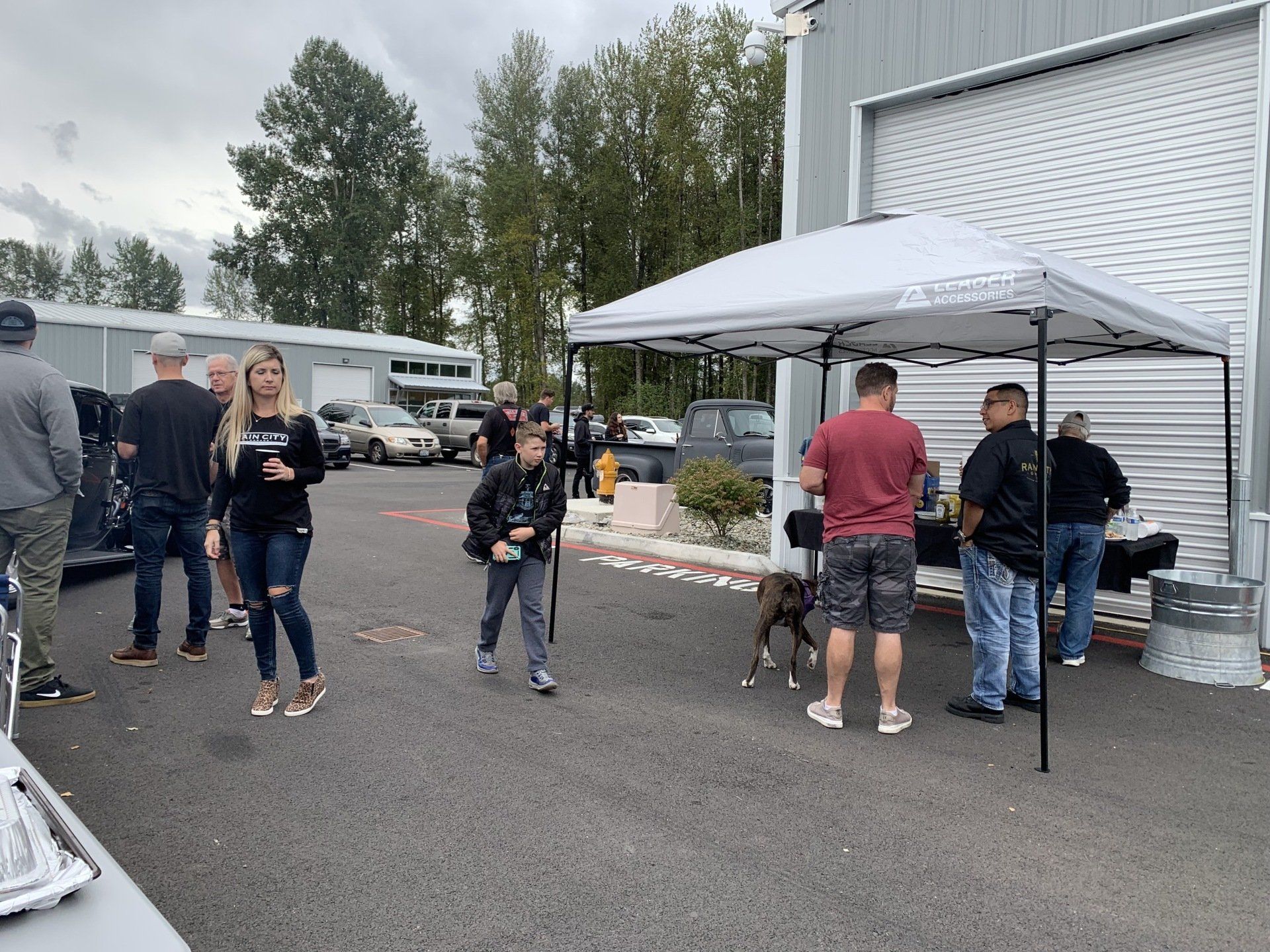 People gathered outside a building under a white canopy, chatting near tables and a grill.