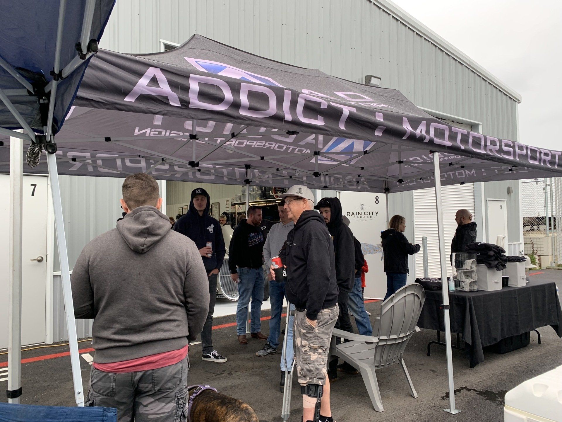 People gathered under a black “Addictive” canopy tent at an outdoor event.