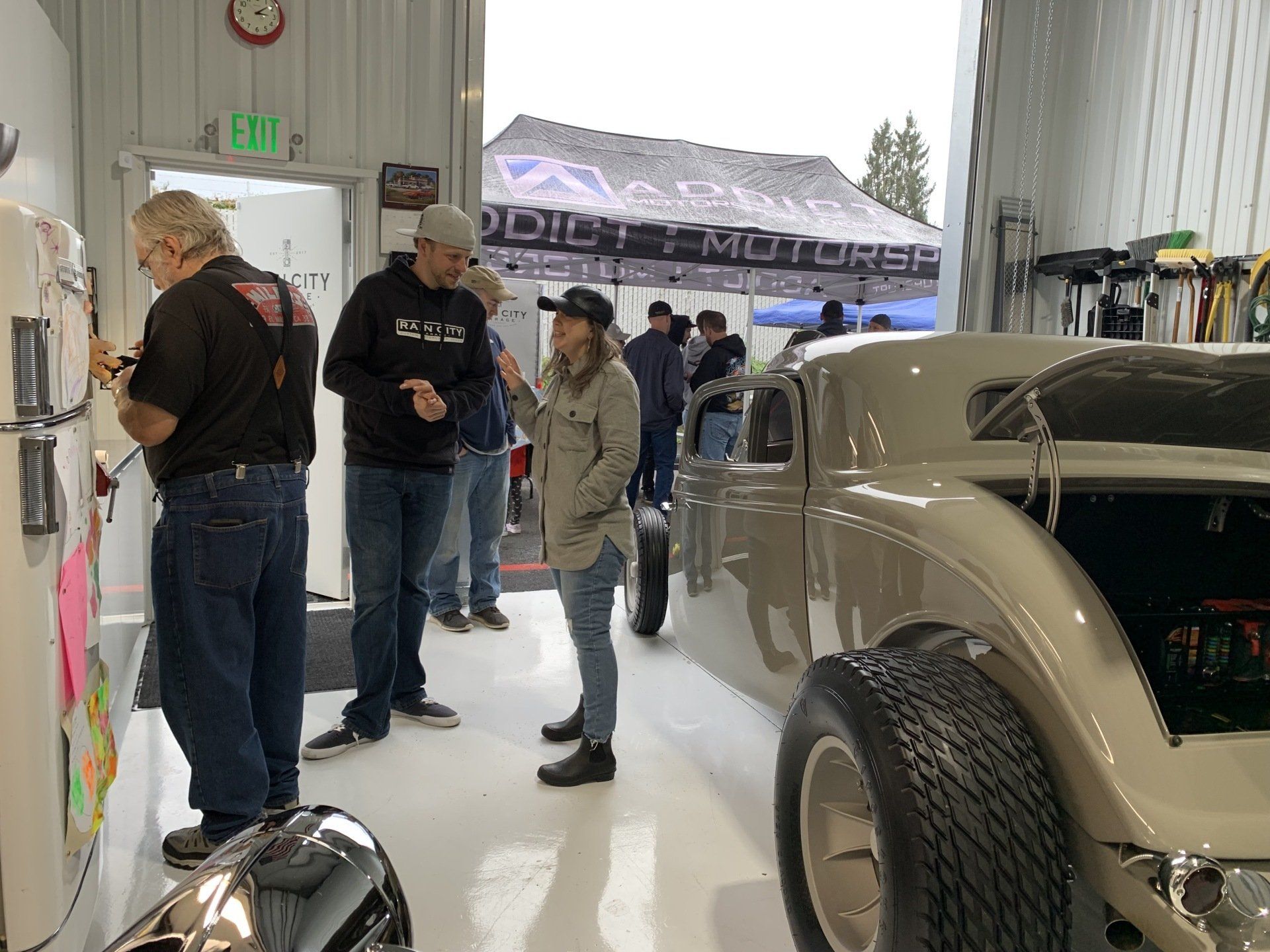 Classic car show inside a garage, with people chatting beside a beige vintage car.