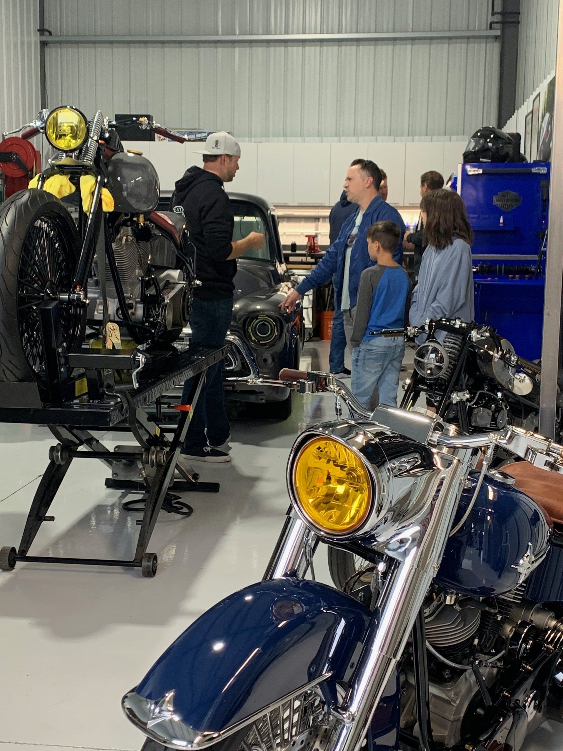 Motorcycles in a workshop with three people talking beside them.