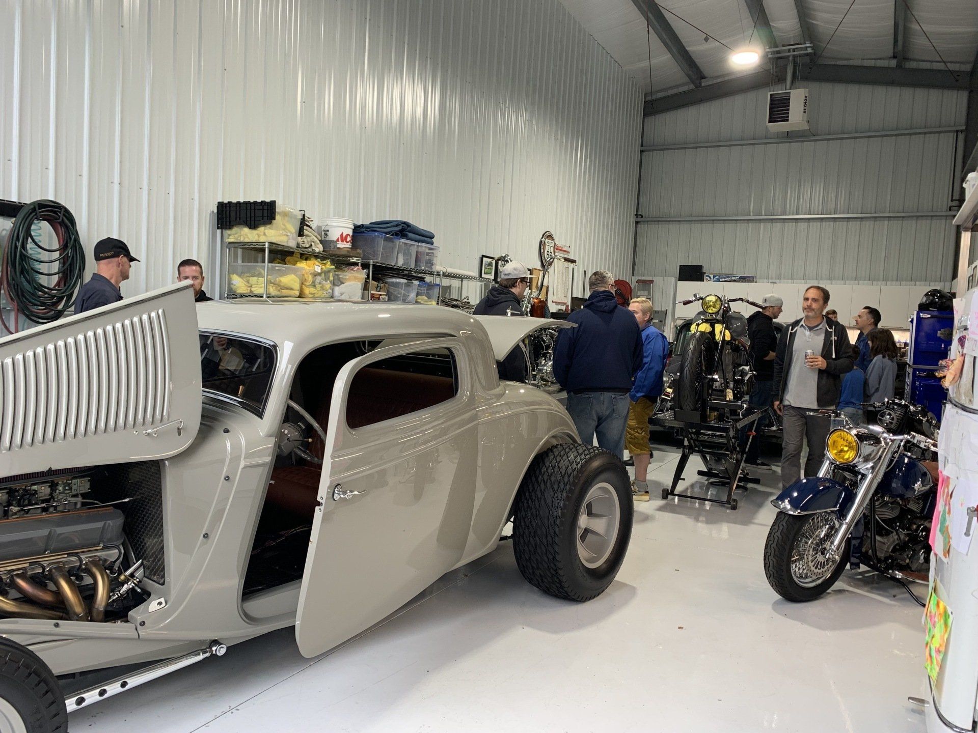 Classic hot rod in a garage with people and motorcycles nearby