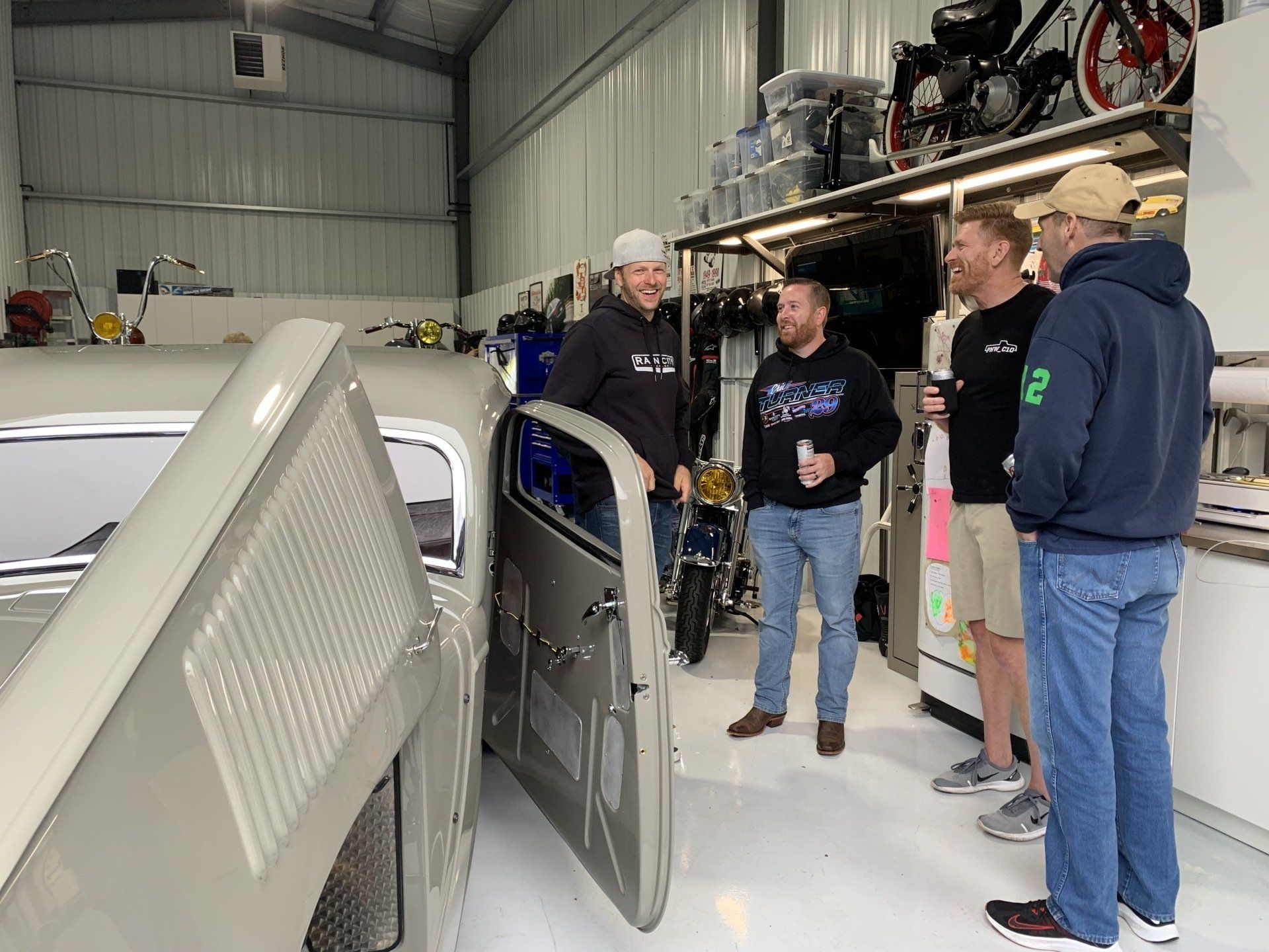 People gathered in a workshop beside a car with its hood open, discussing the engine.