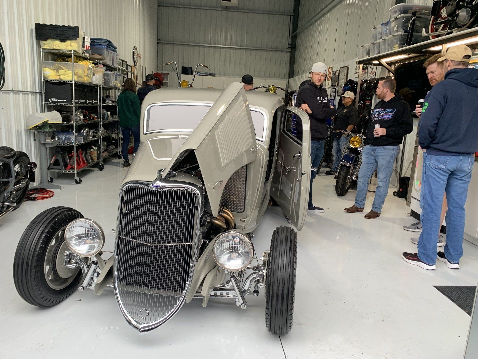 Vintage hot rod in a garage, with several people gathered around it.